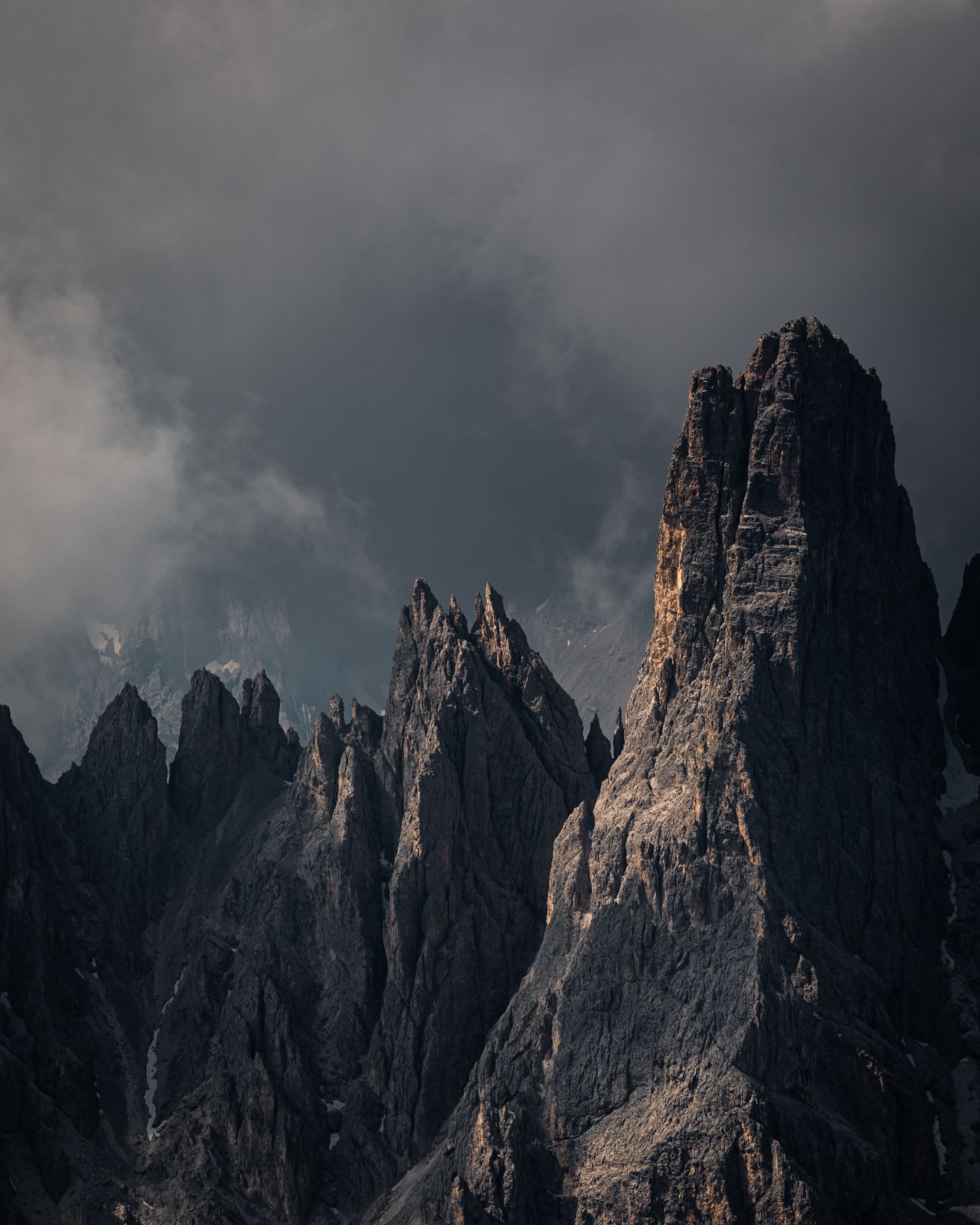 Jagged, rocky peaks pierce a dark, ominous sky, wispy clouds racing above them.