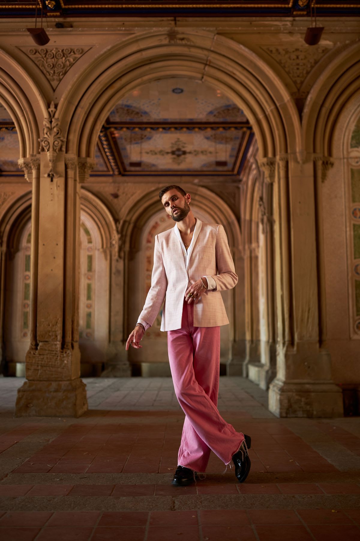 A man in pink clothes is cross-legged and staring straight ahead and he is in an environment with ancient architecture