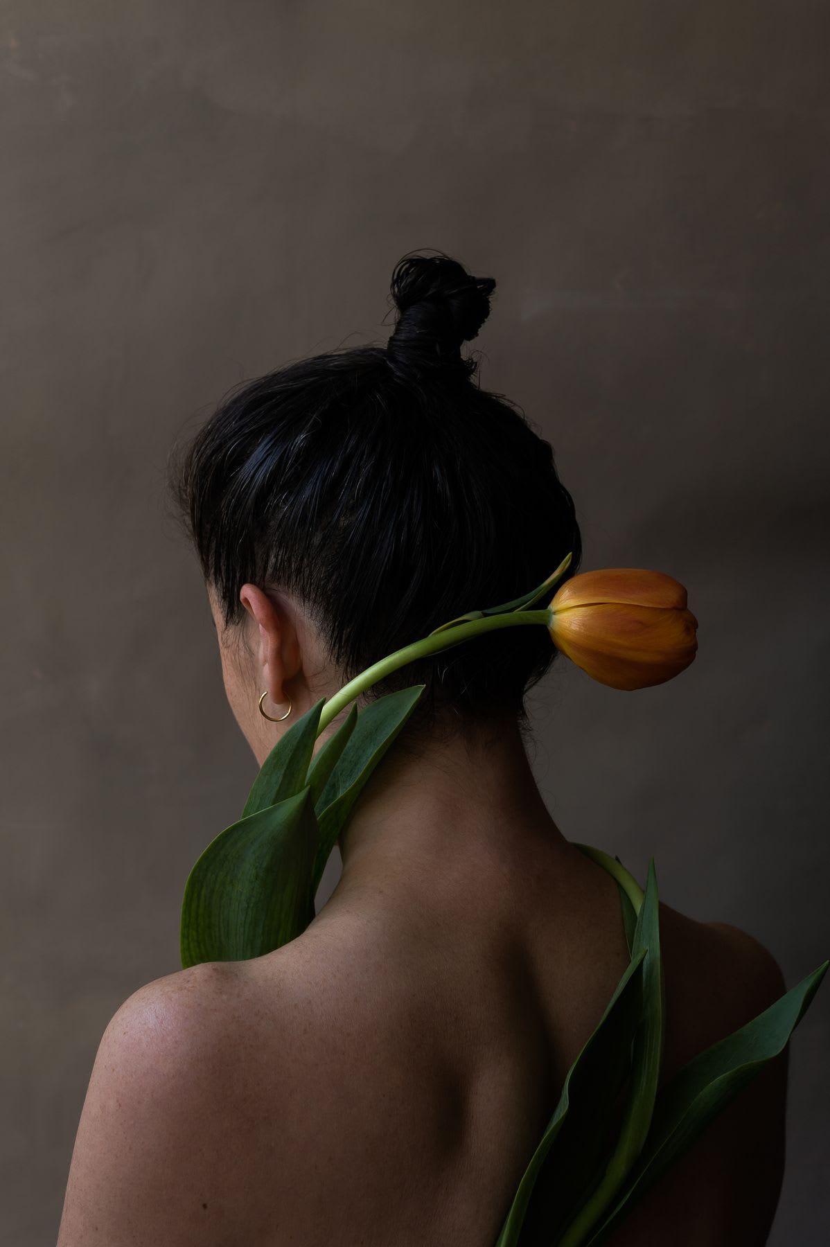Woman standing with stem and leaves wrapped around her bare body and the tulip at the back of her head