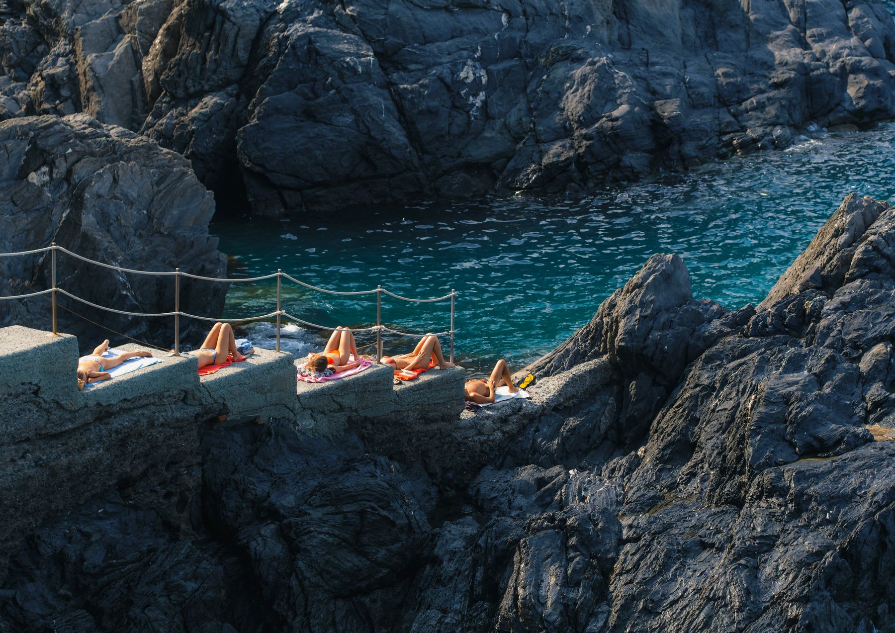 Women in bikinis lying on towels on the steps of a rock by the sea