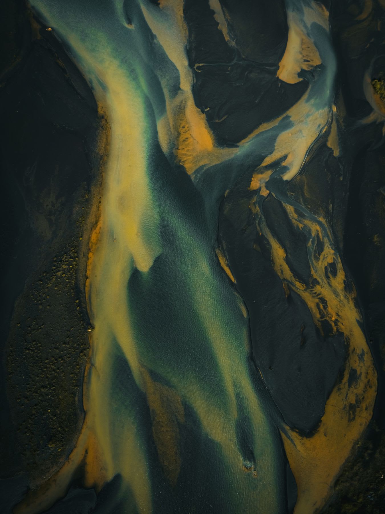 Aerial of a river passing between a lightly forested plain and snowy mountains.