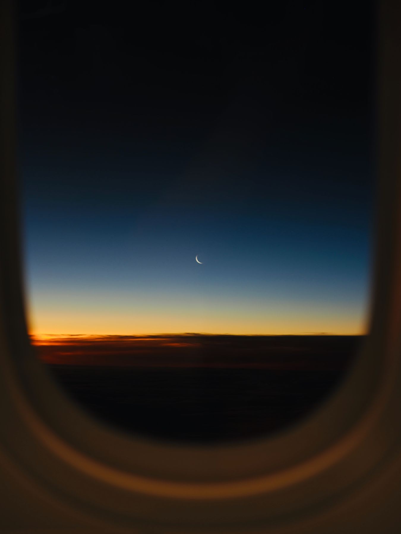 View from an aircraft window of the crescent moon in the sky at dusk