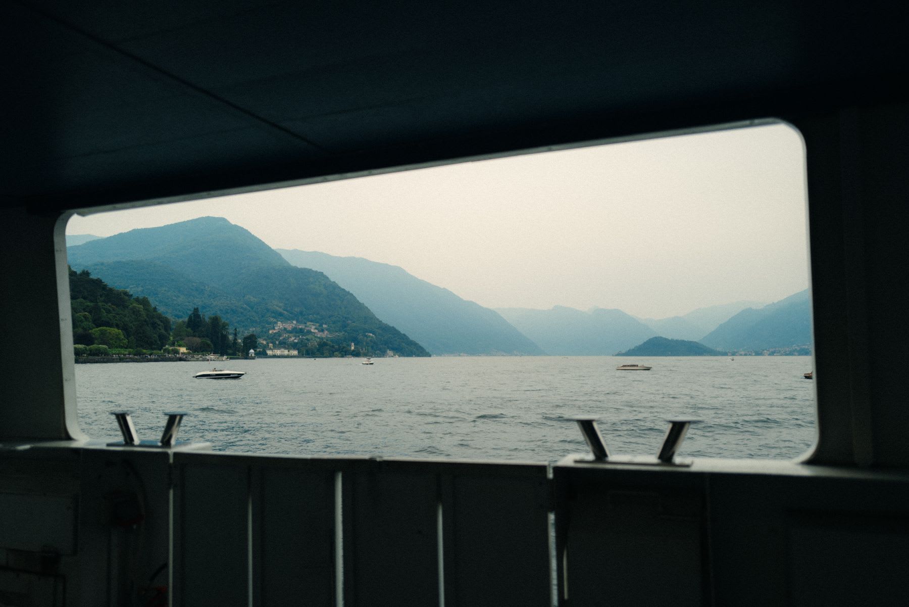 Several boats are seen travelling on a large mountain lake from inside another boat.