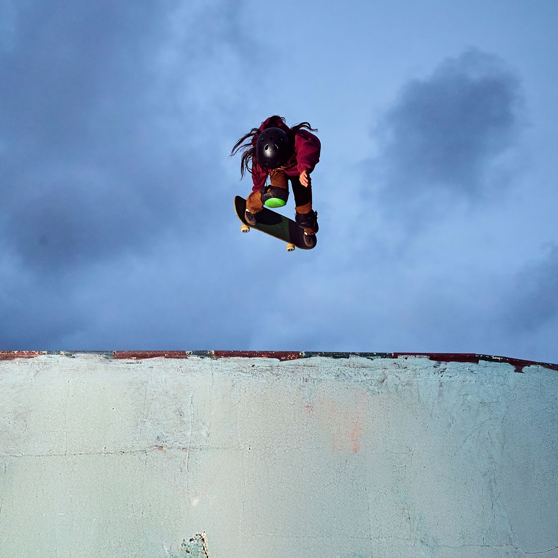 A skateboarder wearing a helmet catches some air while jumping out of a skate ramp against a cloudy sky.