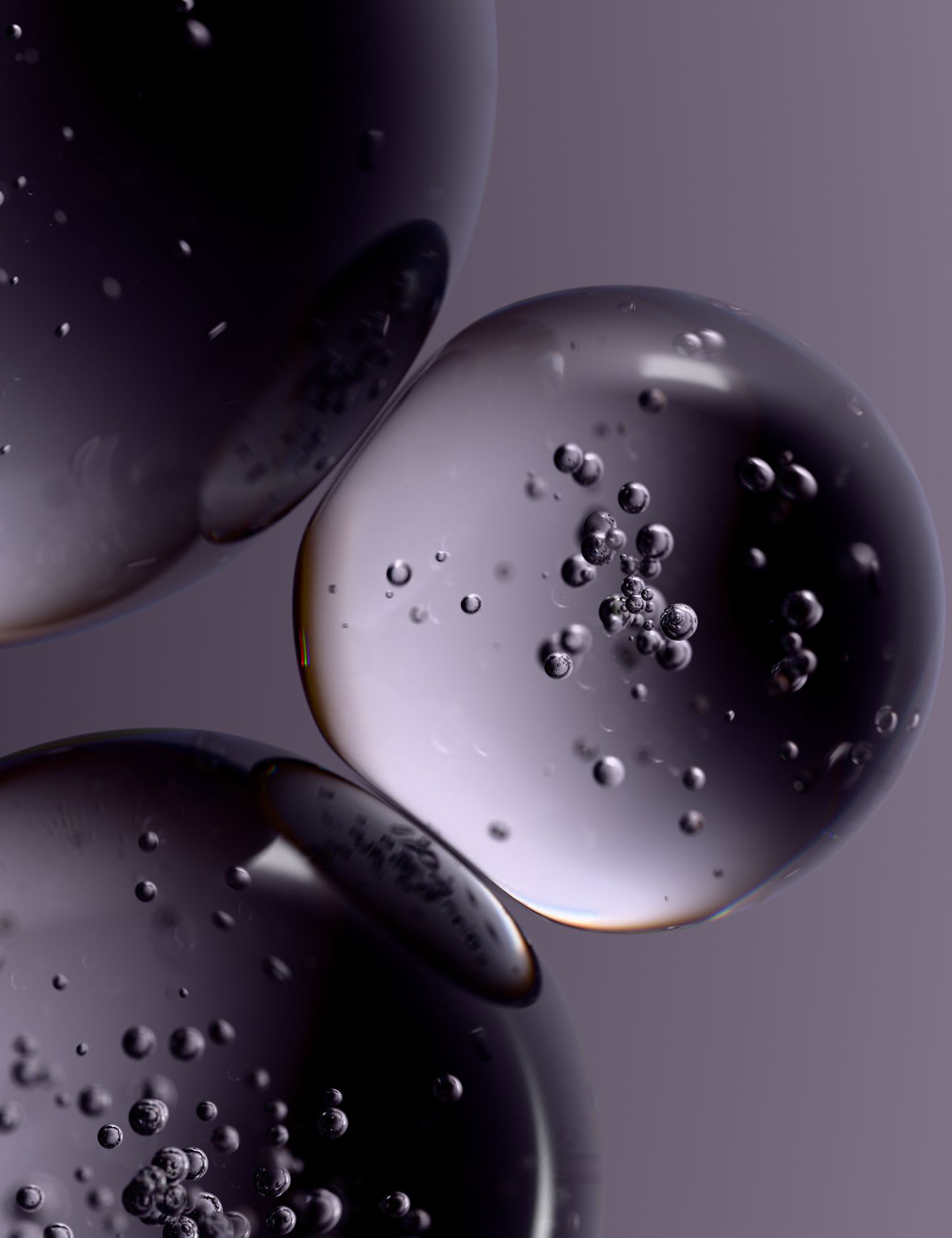A close-up, abstract view of clear liquid spheres filled with smaller bubbles against a muted purple background.