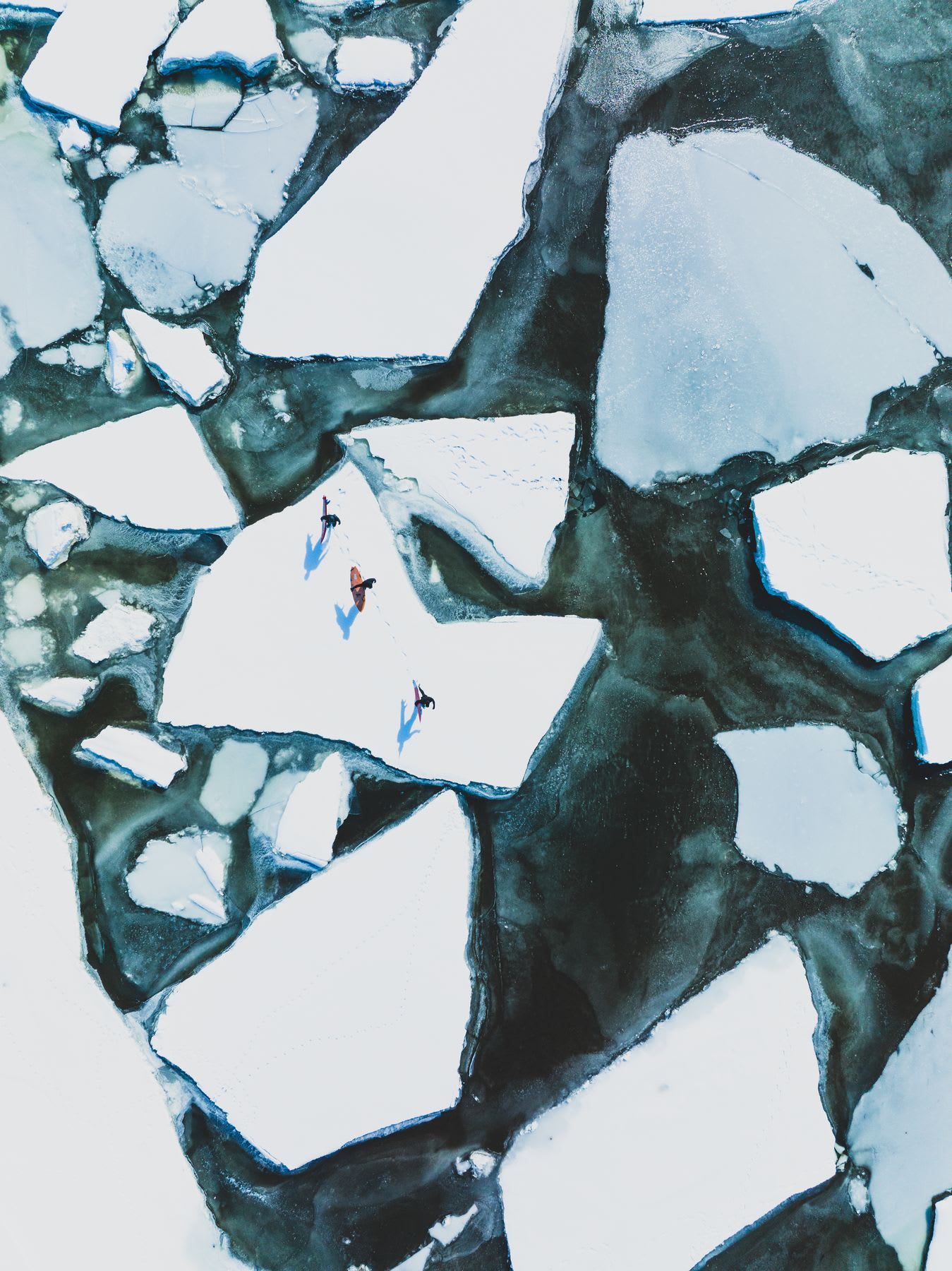 Three people walking on floating ice blocks in a freezing environment, seen from above.