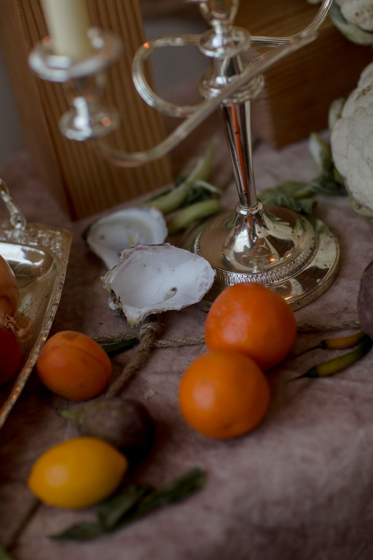 A close-up of a decorative table setting with oranges and shells next to a silver candlestick.