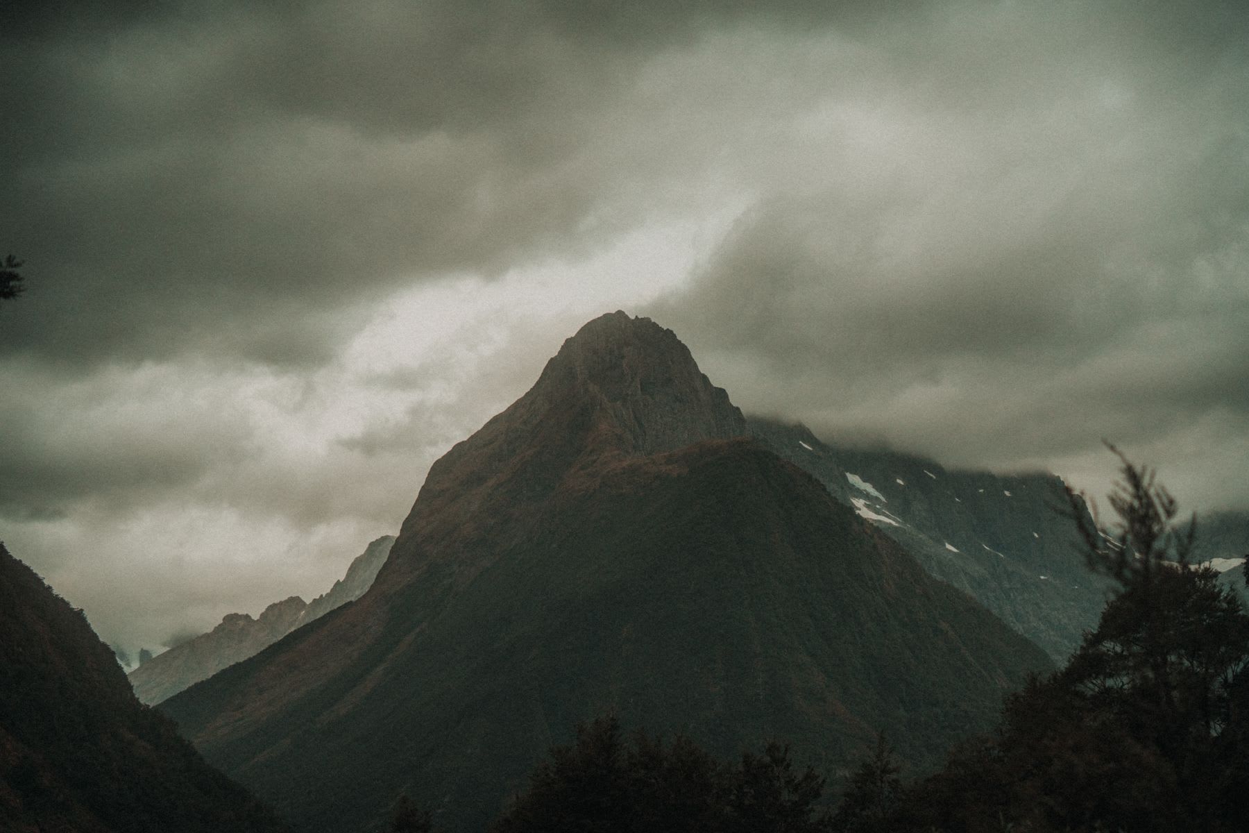 A solitary, rugged mountain peak rises majestically under a brooding, overcast sky, evoking a sense of isolation and natural grandeur.