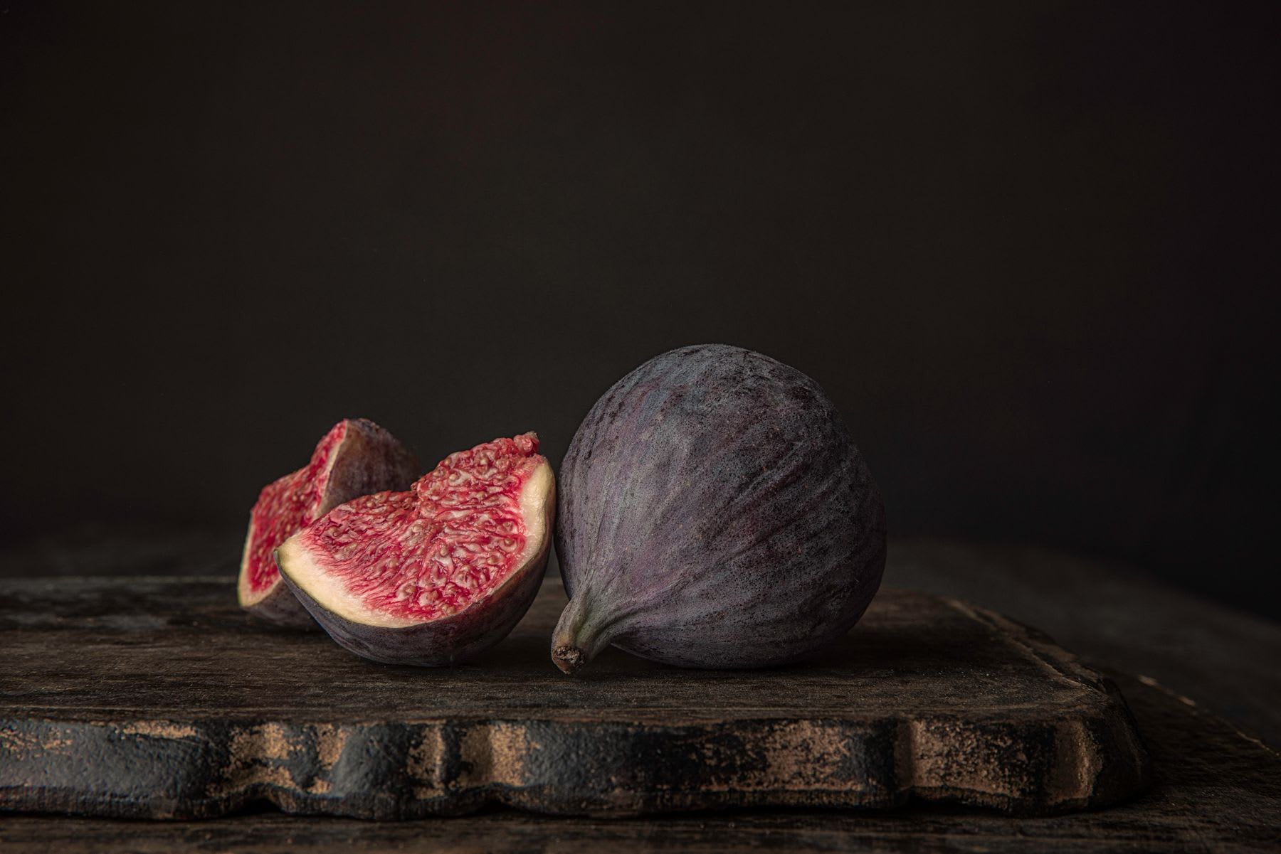 Still life of a whole and halved fig on a rustic wooden surface.
