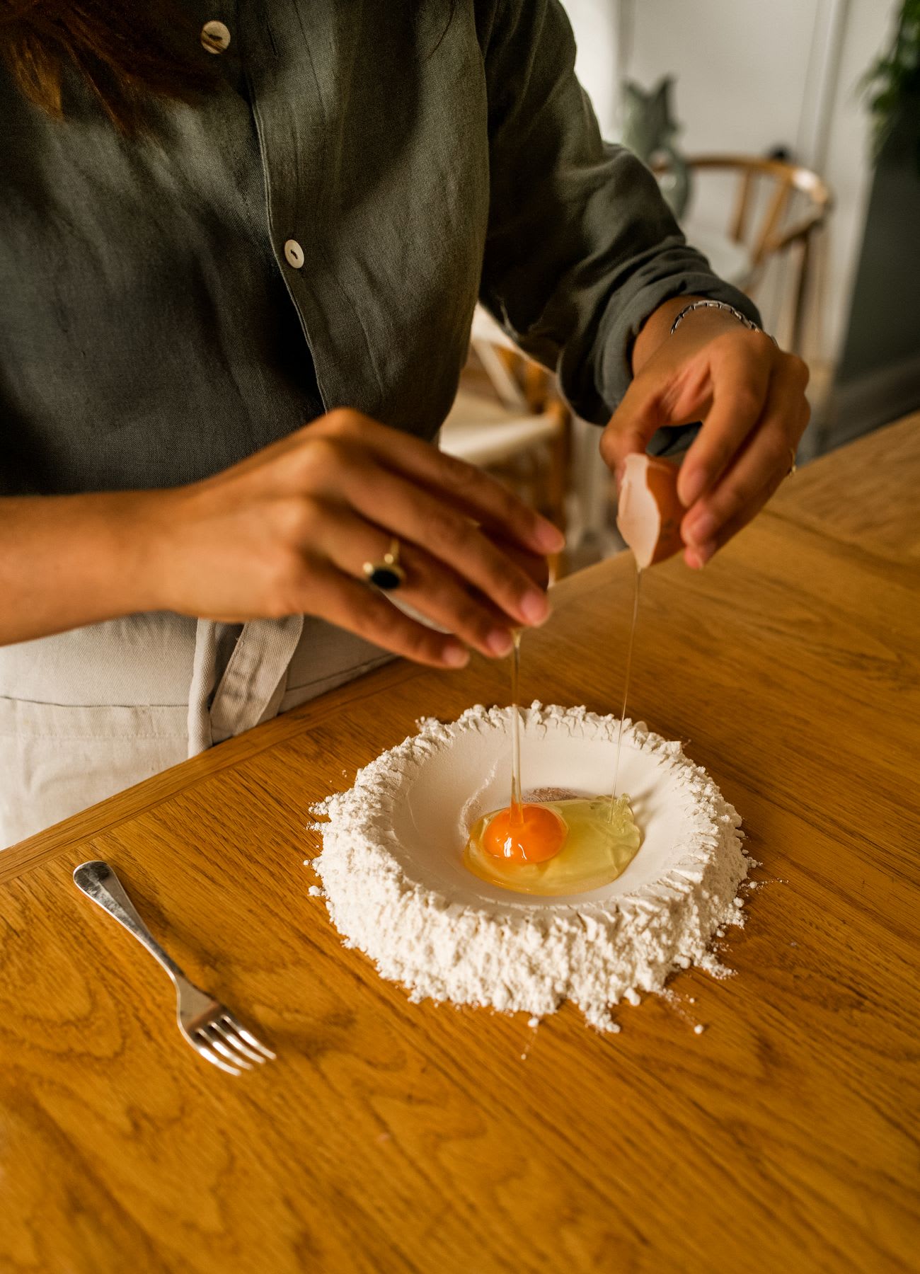 Woman's hands breaking an egg into some wheat flour on a wooden table.
