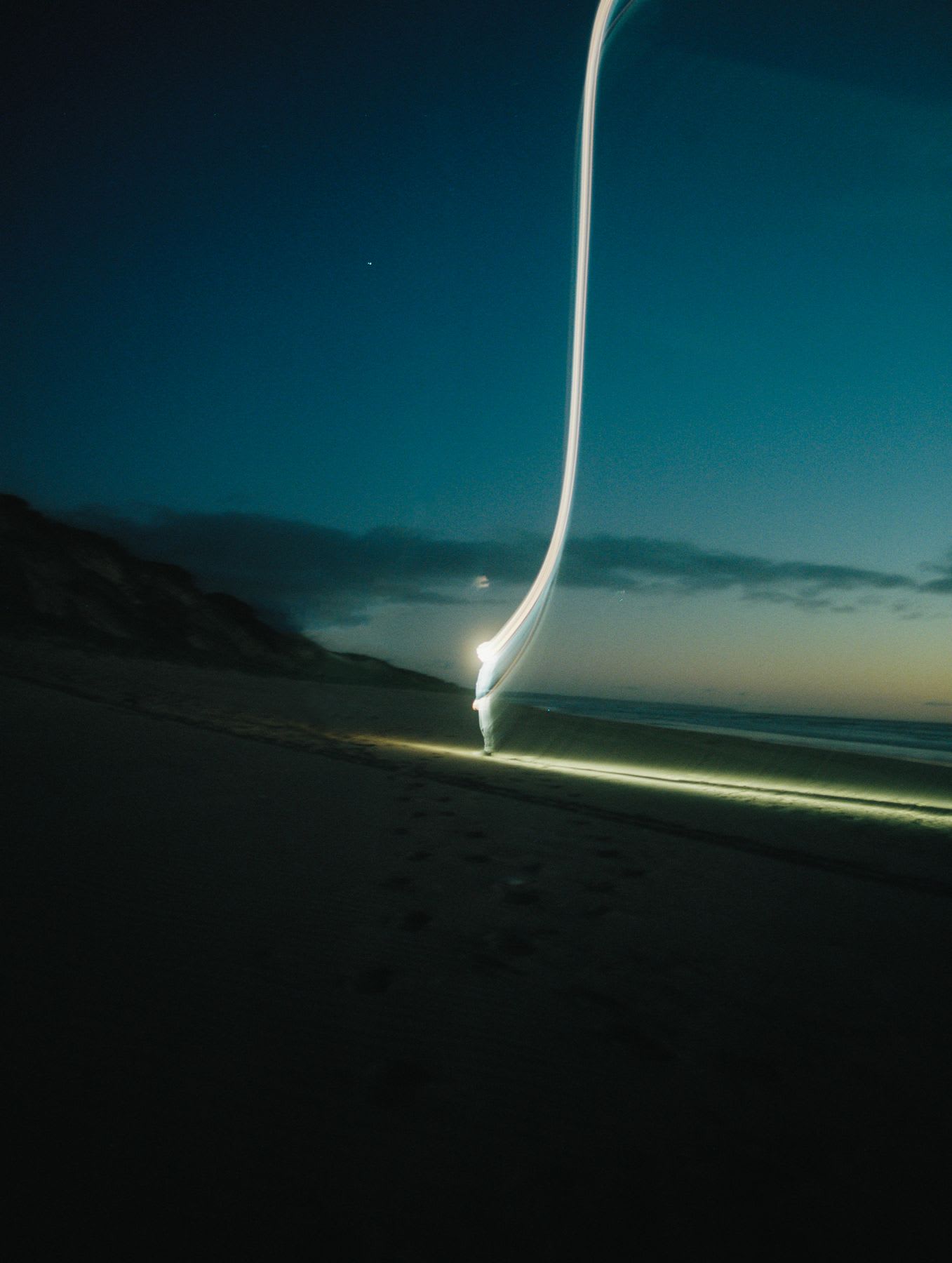 An abstract image of a person standing on a beach enveloped in bright light that is ascending to the sky