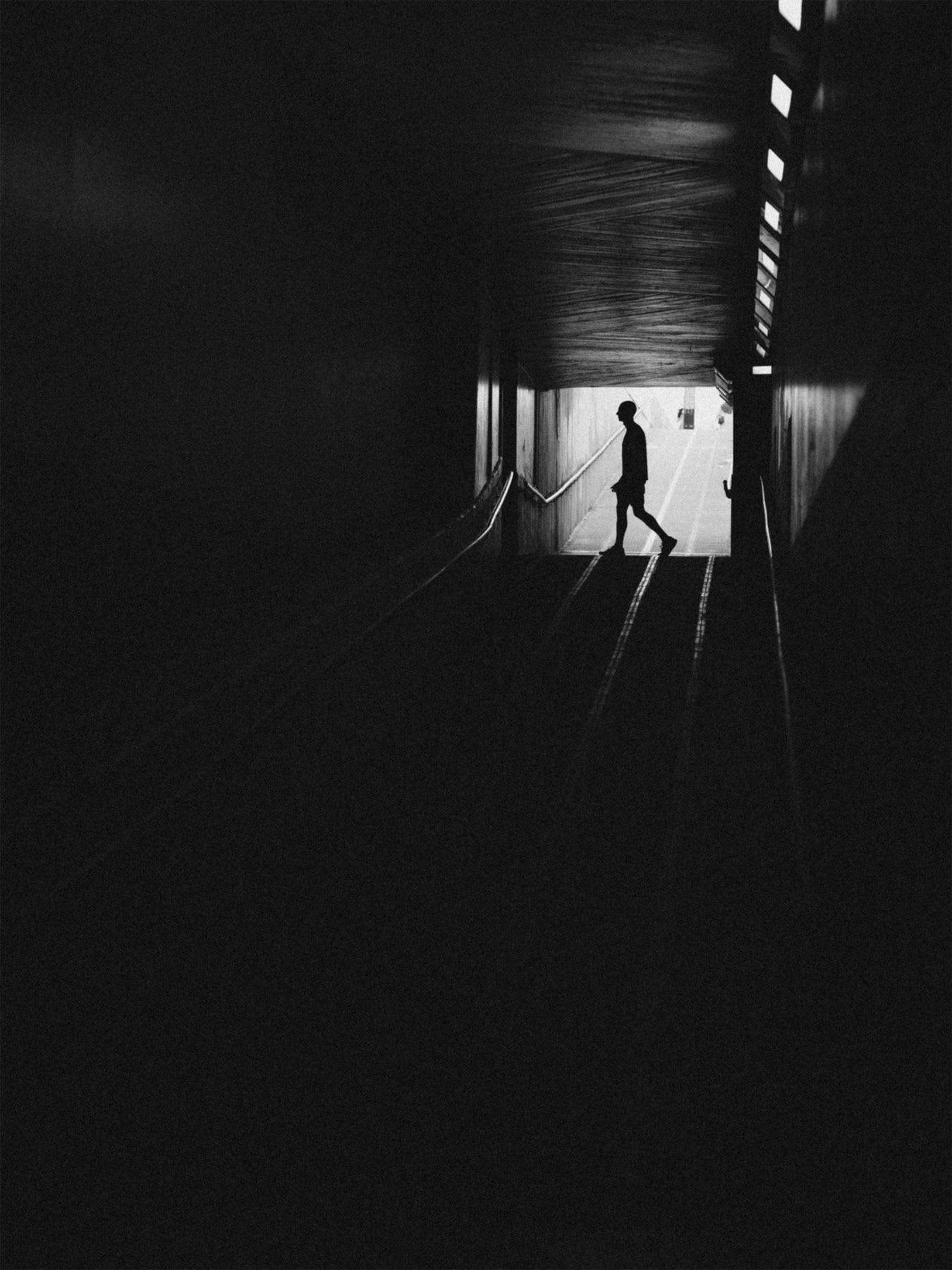 a person walking down a set of stairs in a dark tunnel, with light coming from the other end.
