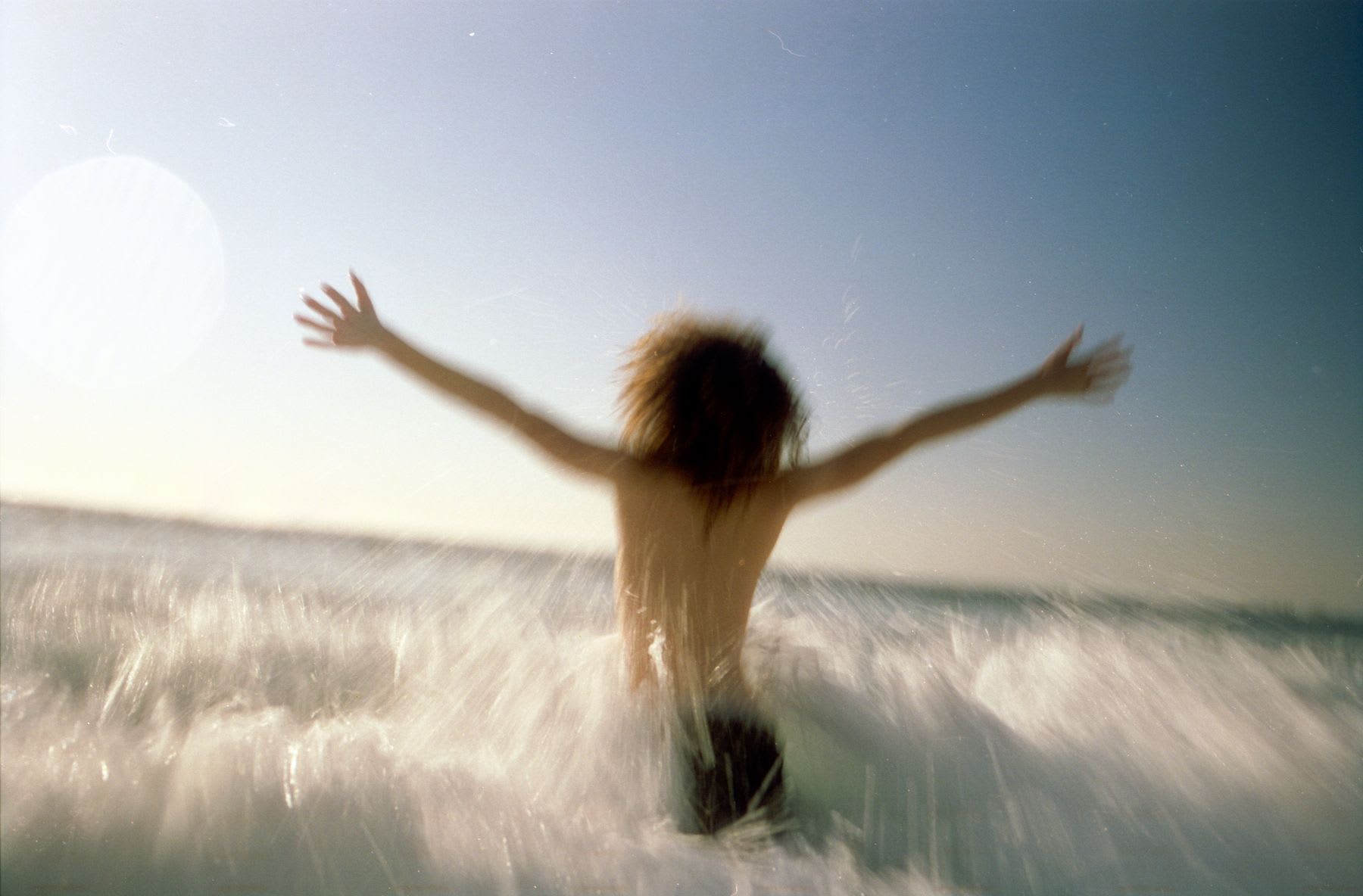 A person with outstretched arms running into the ocean waves.