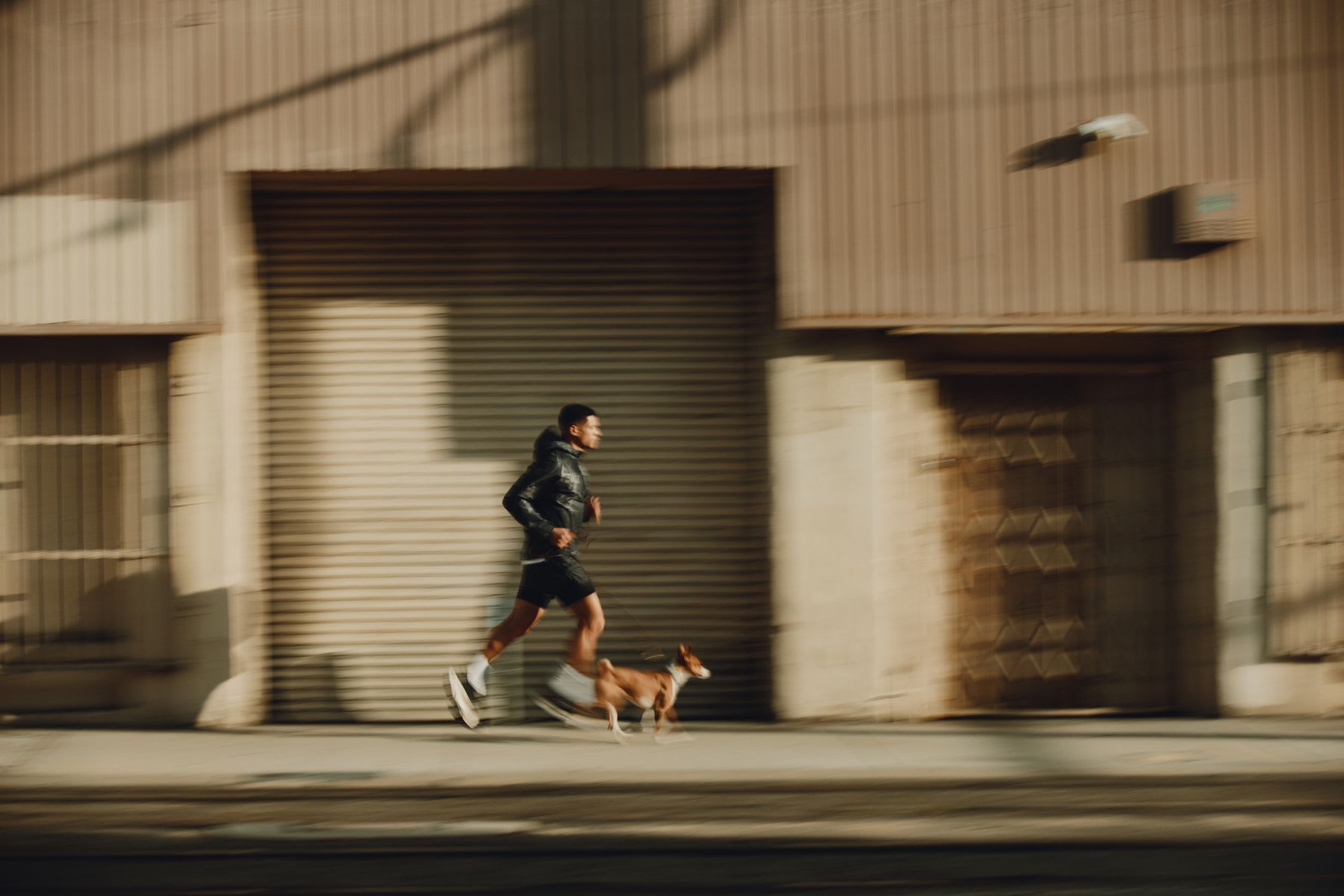 Man running on a city sidewalk with his dog by his side