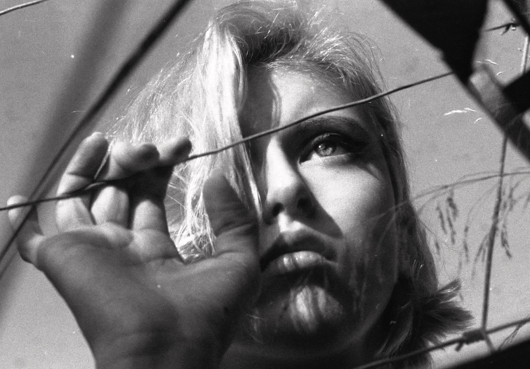 A young woman looking sad as she touches and gazes through a wire fence.