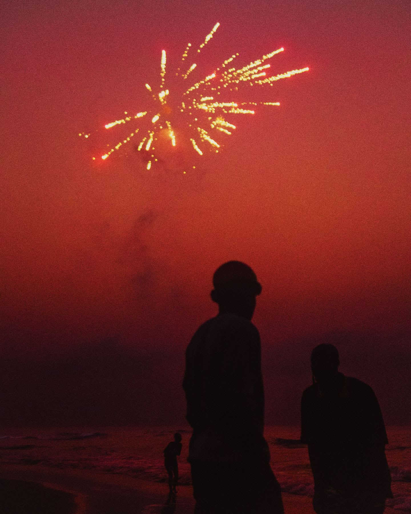 Silhouettes of people on the beach at dusk with fireworks in the sky.