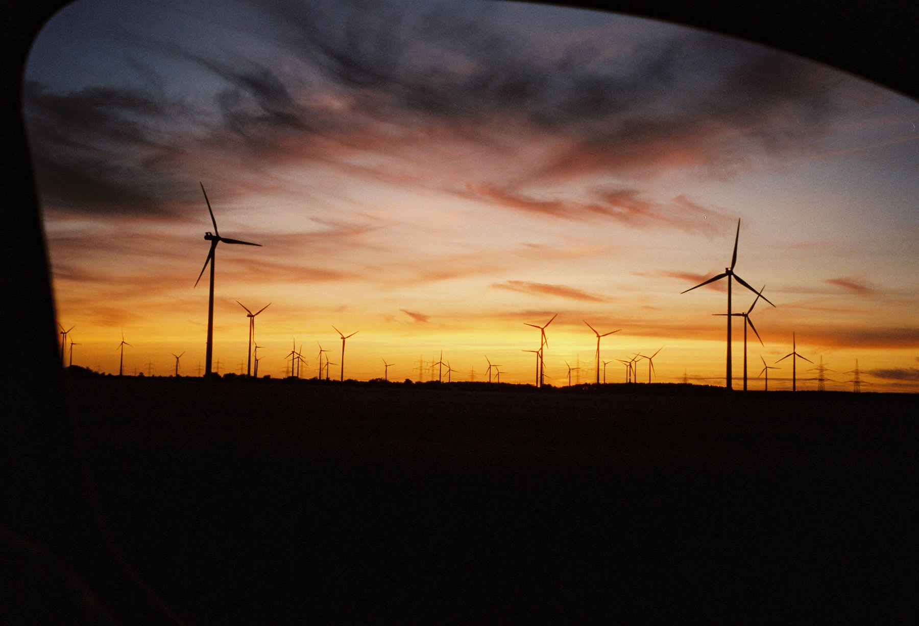 Wind turbines silhouetted against a vibrant sunset sky, viewed from inside a vehicle.