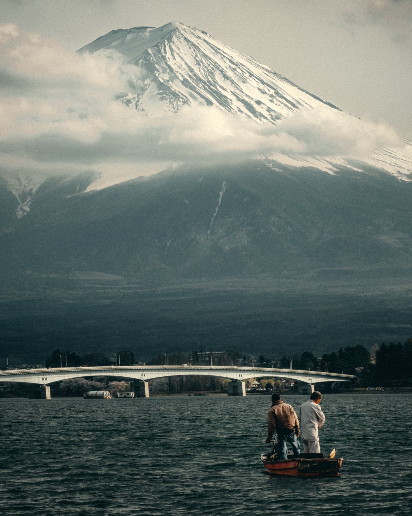 Mount fuji in Japan, a partially cloudy day, two men are in a boat on the water.