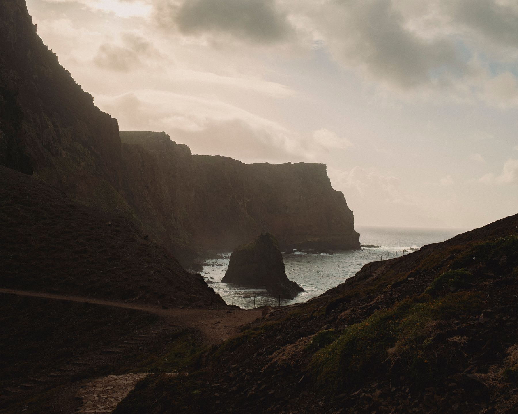 A bay beach under a cliff, with a rock formation in an ocean.