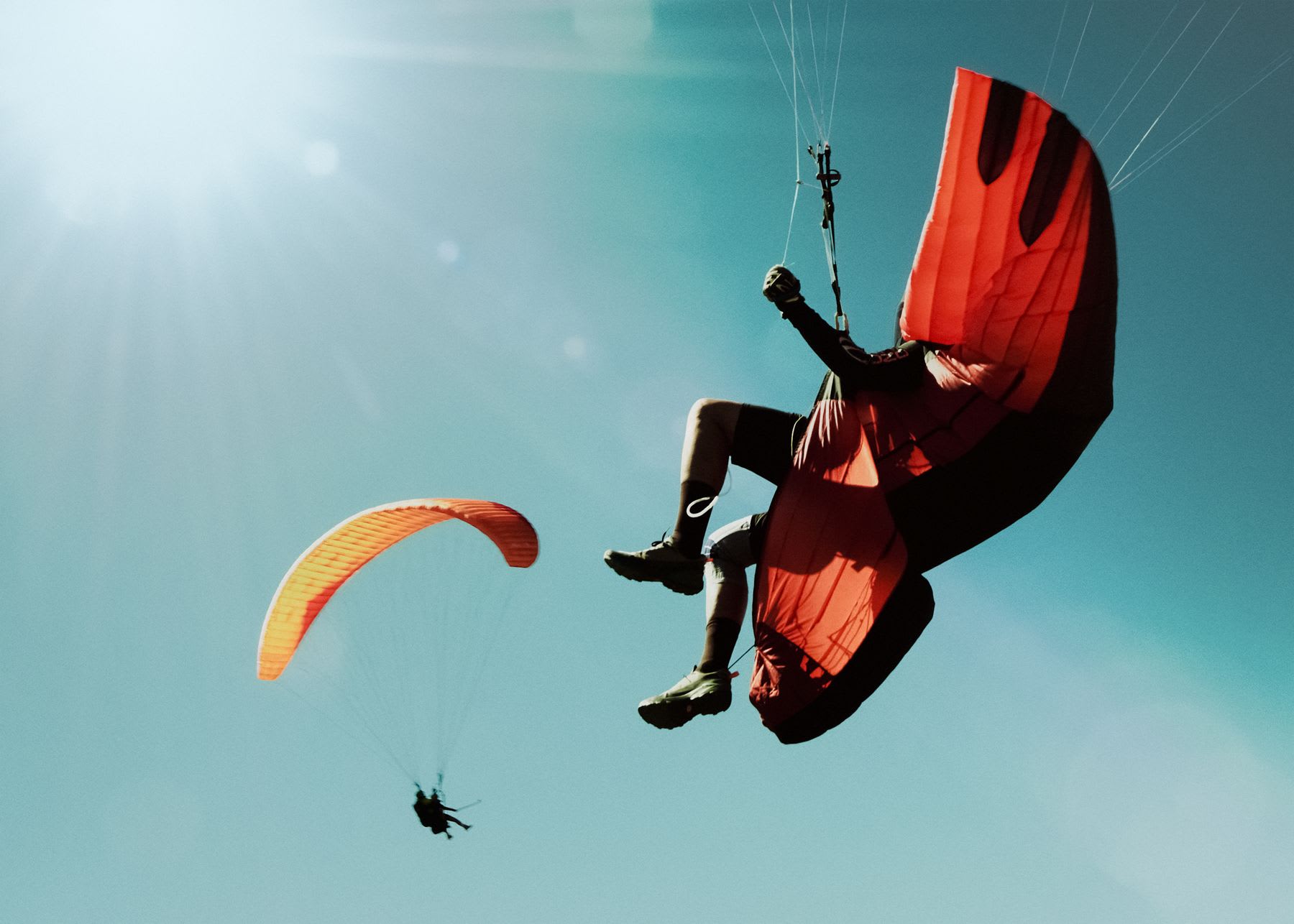 Two people paragliding with colorful parachutes high in a clear blue sky filled with bright sunlight.
