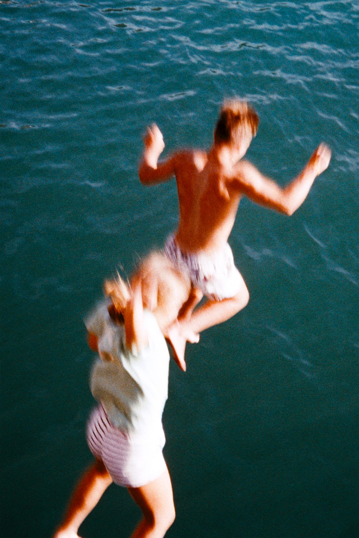 Two people in mid-air jumping towards the sea