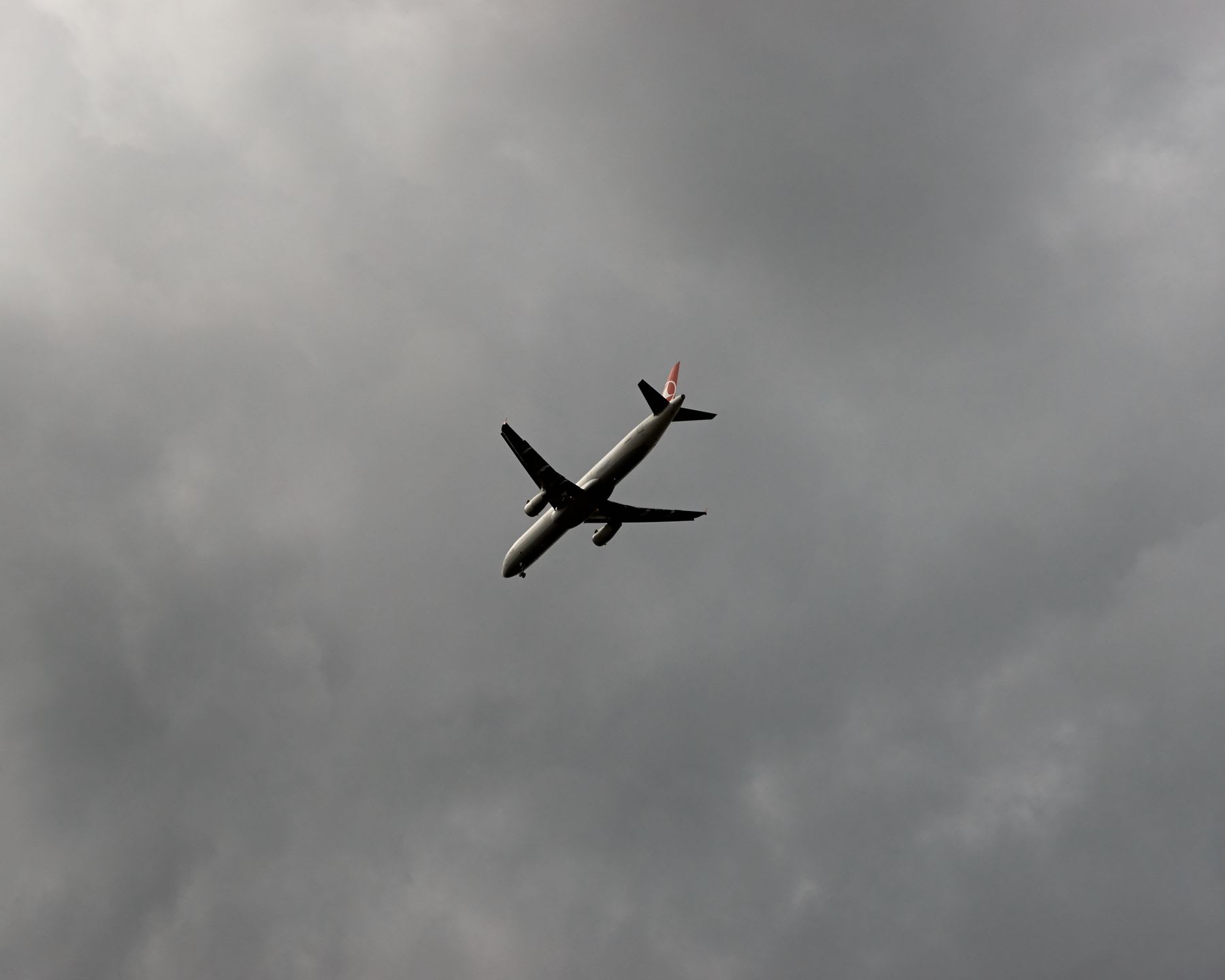 A commercial airliner flies high above in the sky on a cloudy and gray day.