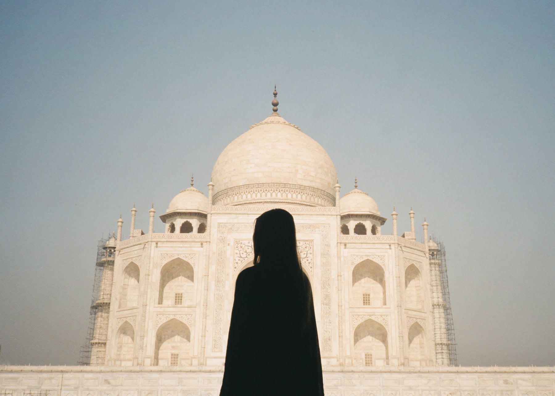 Silhouette of a person standing in front of the Taj Mahal on a clear day.