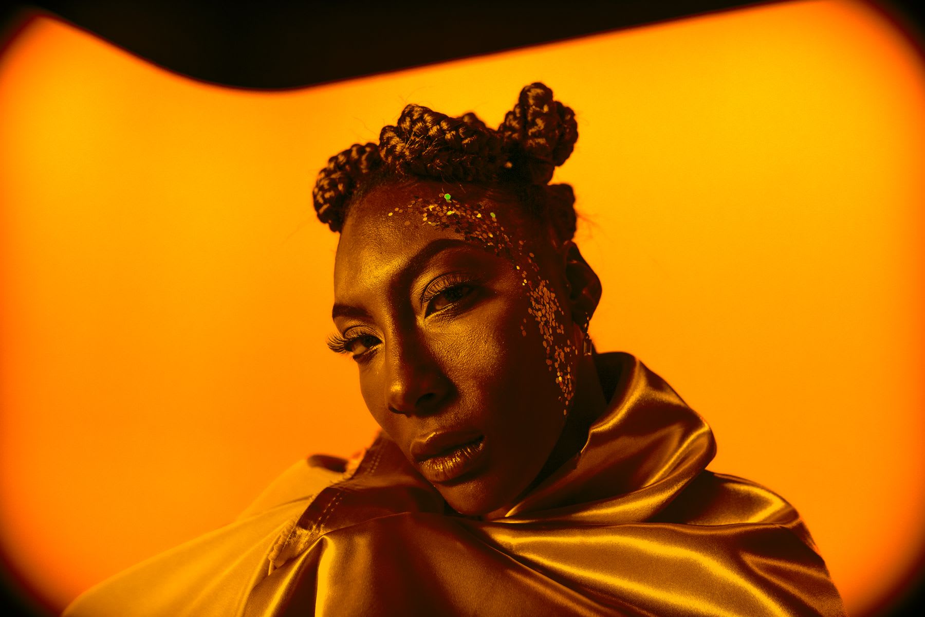 Woman with glitter on her face posing for a photo in a golden room