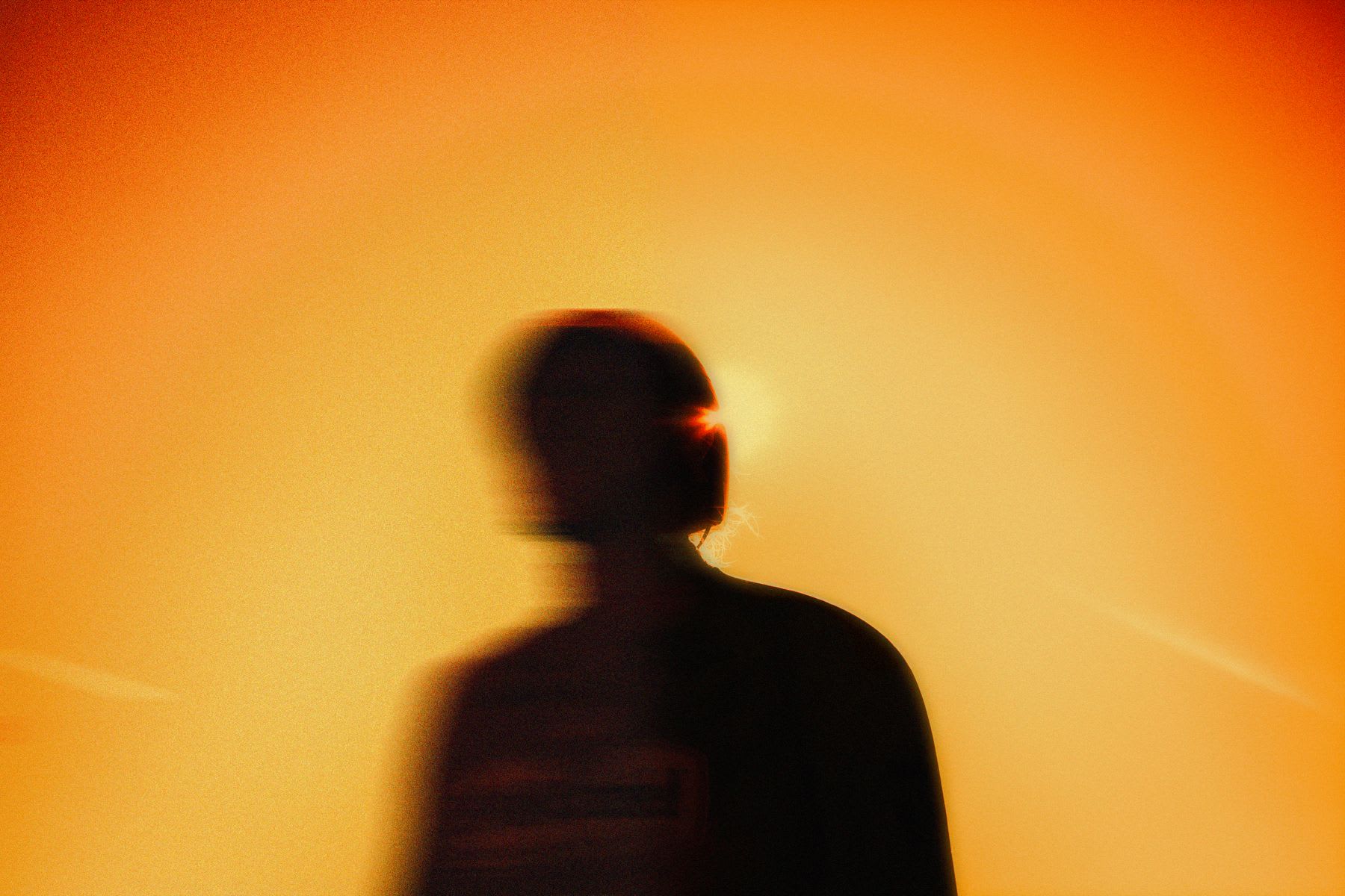 A motion-blurred silhouette of a person is captured against a warm, grainy orange background with a bright light flare.