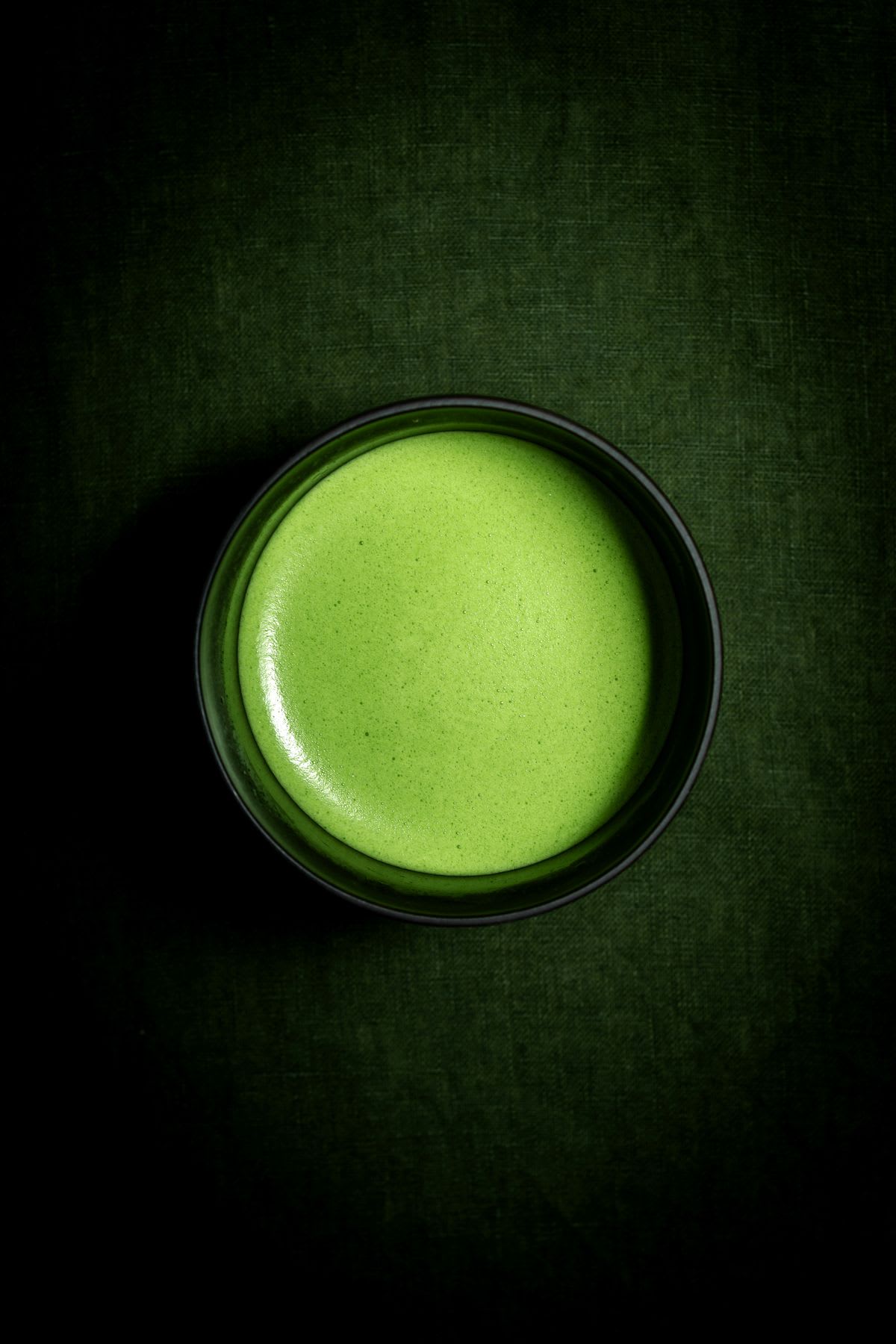 Bowl with a frothy green tea liquid against a dark green tablecloth.