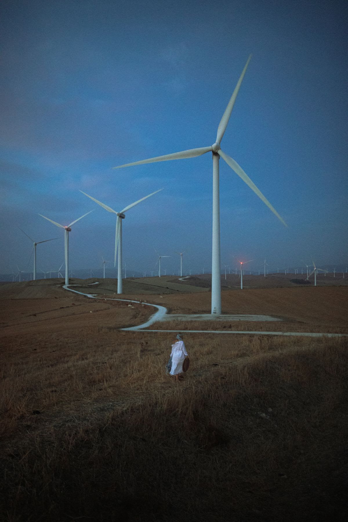 Woman walks through field toward the road leading past wind turbines on a foggy day.