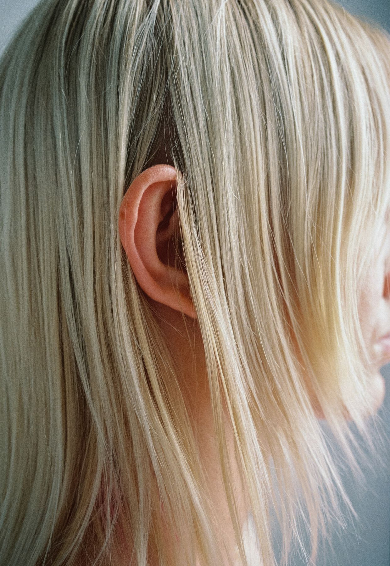 A close-up shot of a person's ear, framed by their straight, light blonde hair.