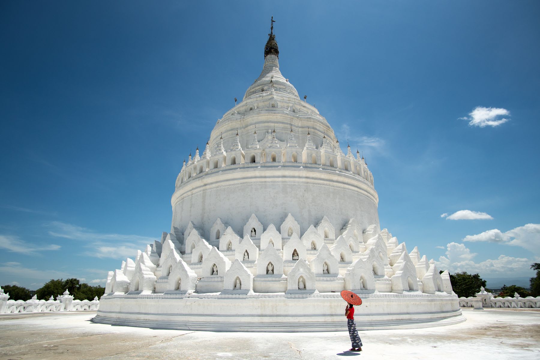 A large white temple under a blue sky with scattered clouds, with a person in red looking up at the structure.