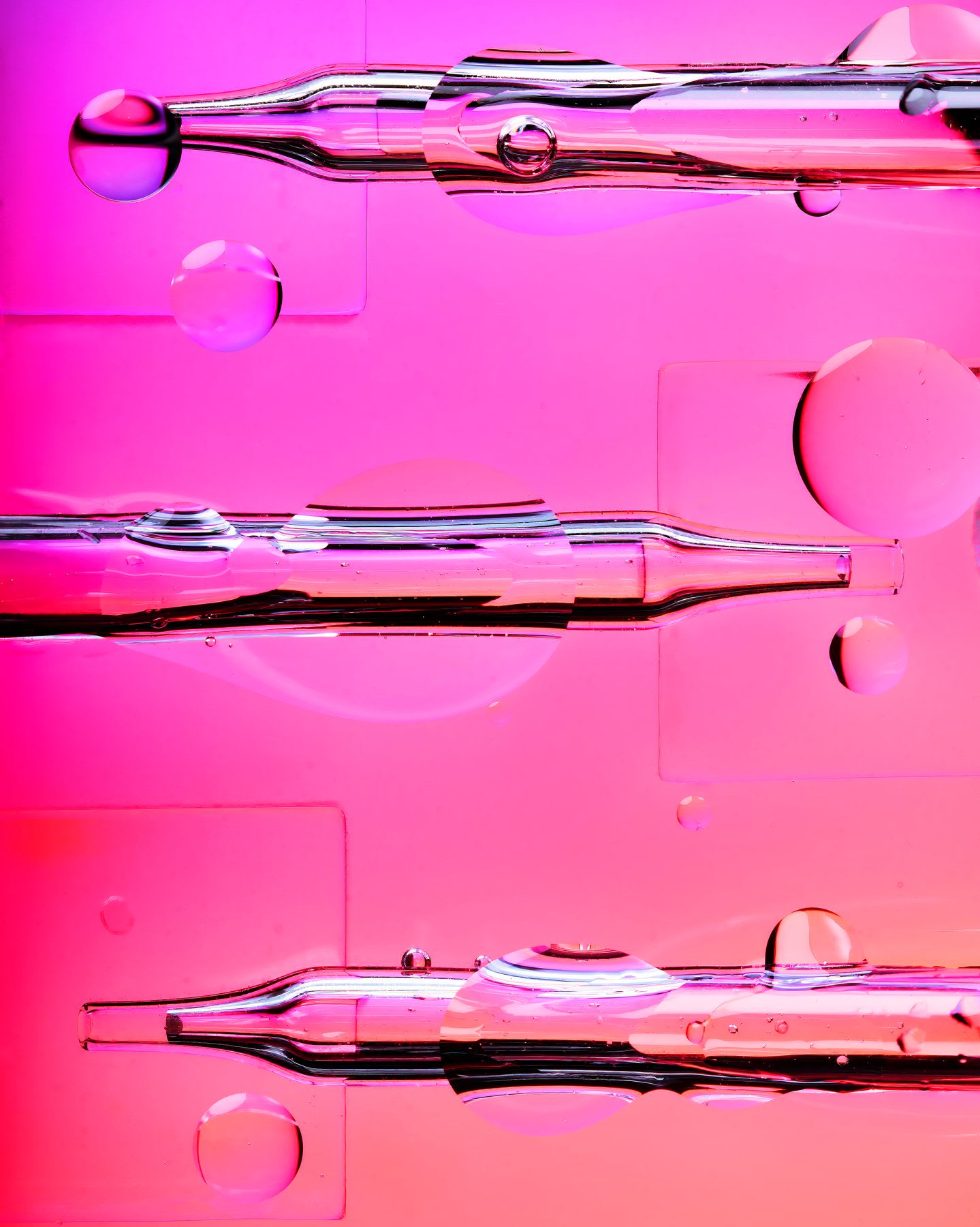 Abstract view of three glass pipettes and transparent bubbles against a vibrant pink background.