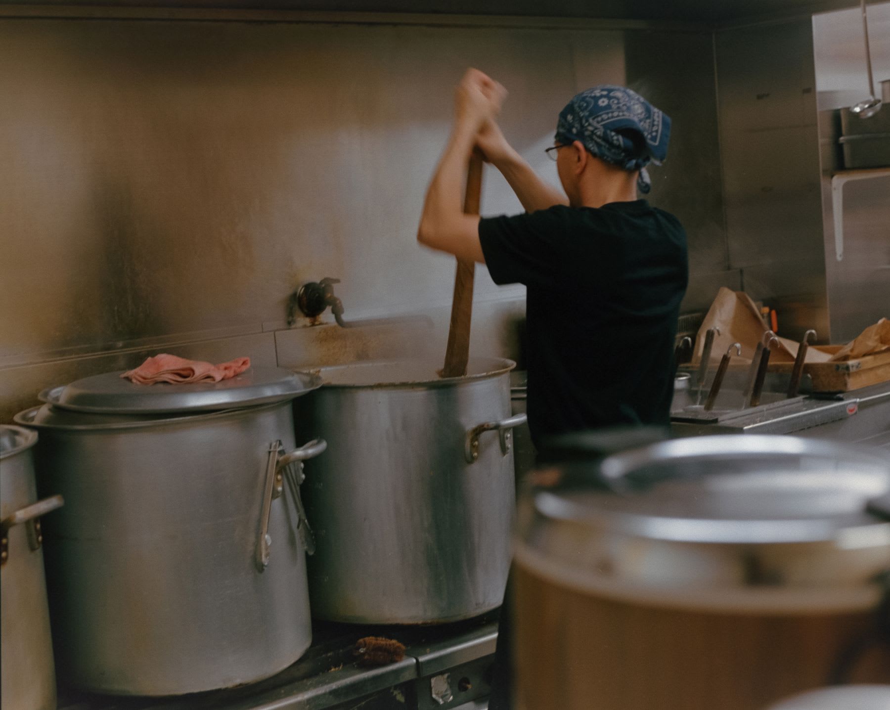 A person has their back turned and is stirring a large pan in a kitchen