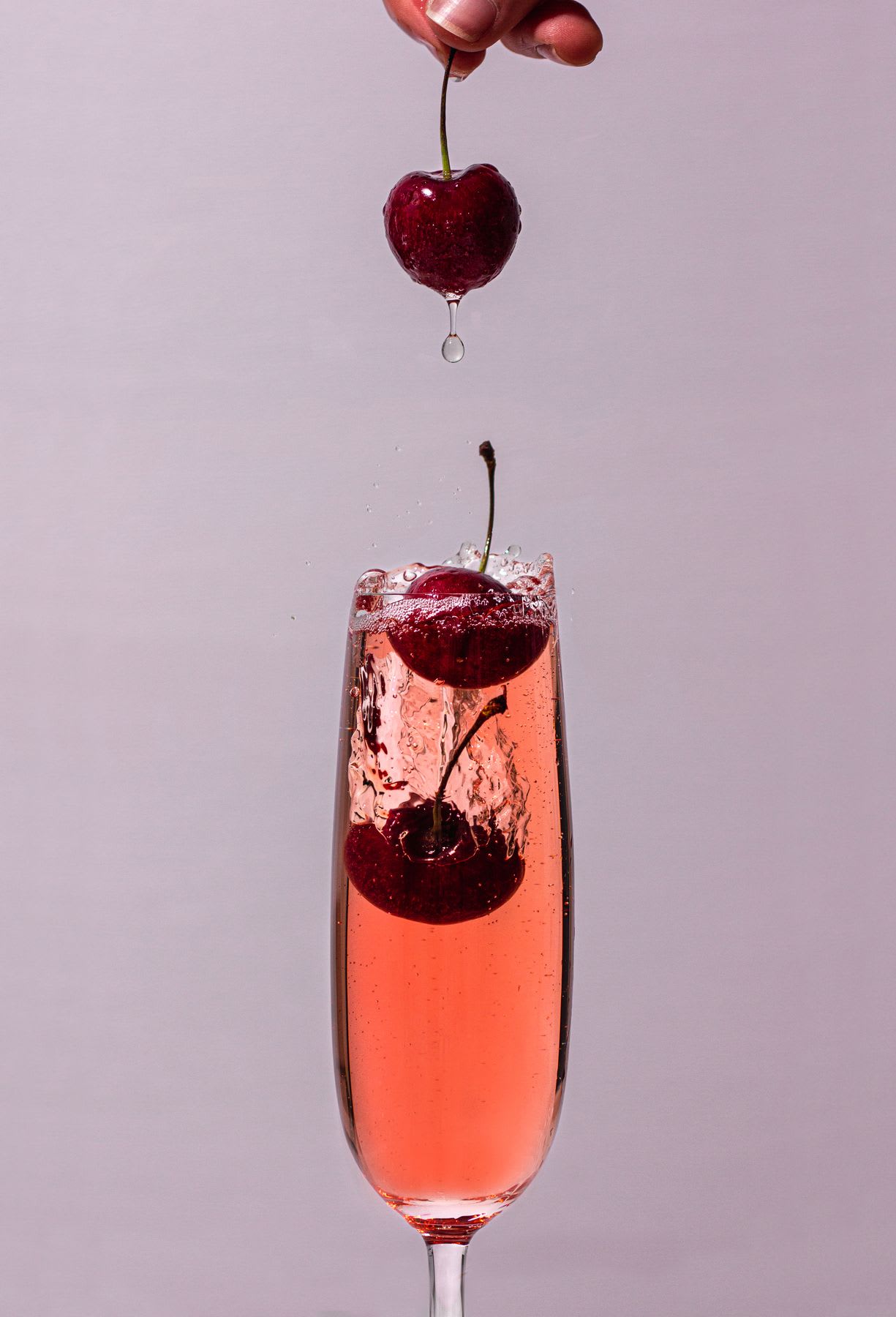 Close up of hand dropping cherry into glass of drink
