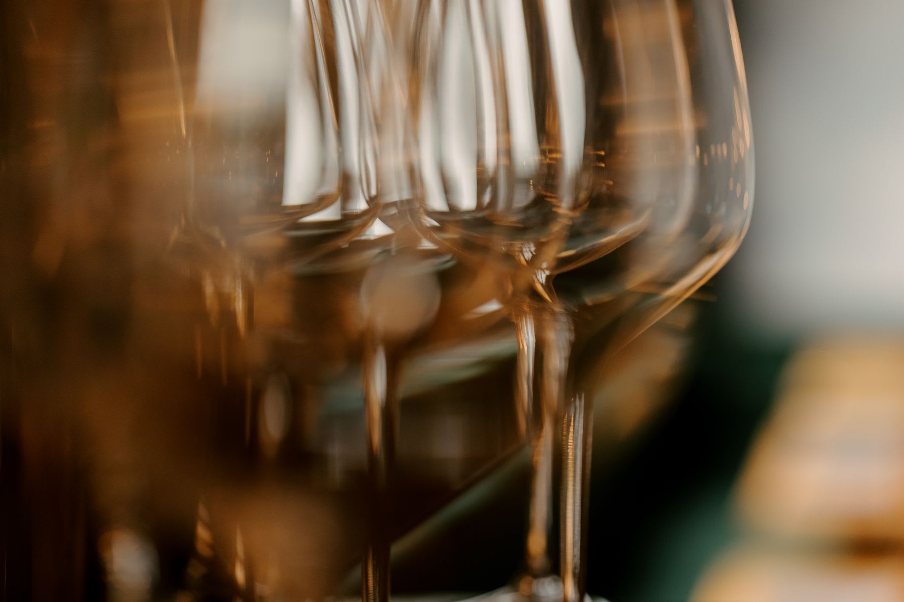 An artistic, abstract close-up of a row of empty wine glasses reflecting warm, golden light.