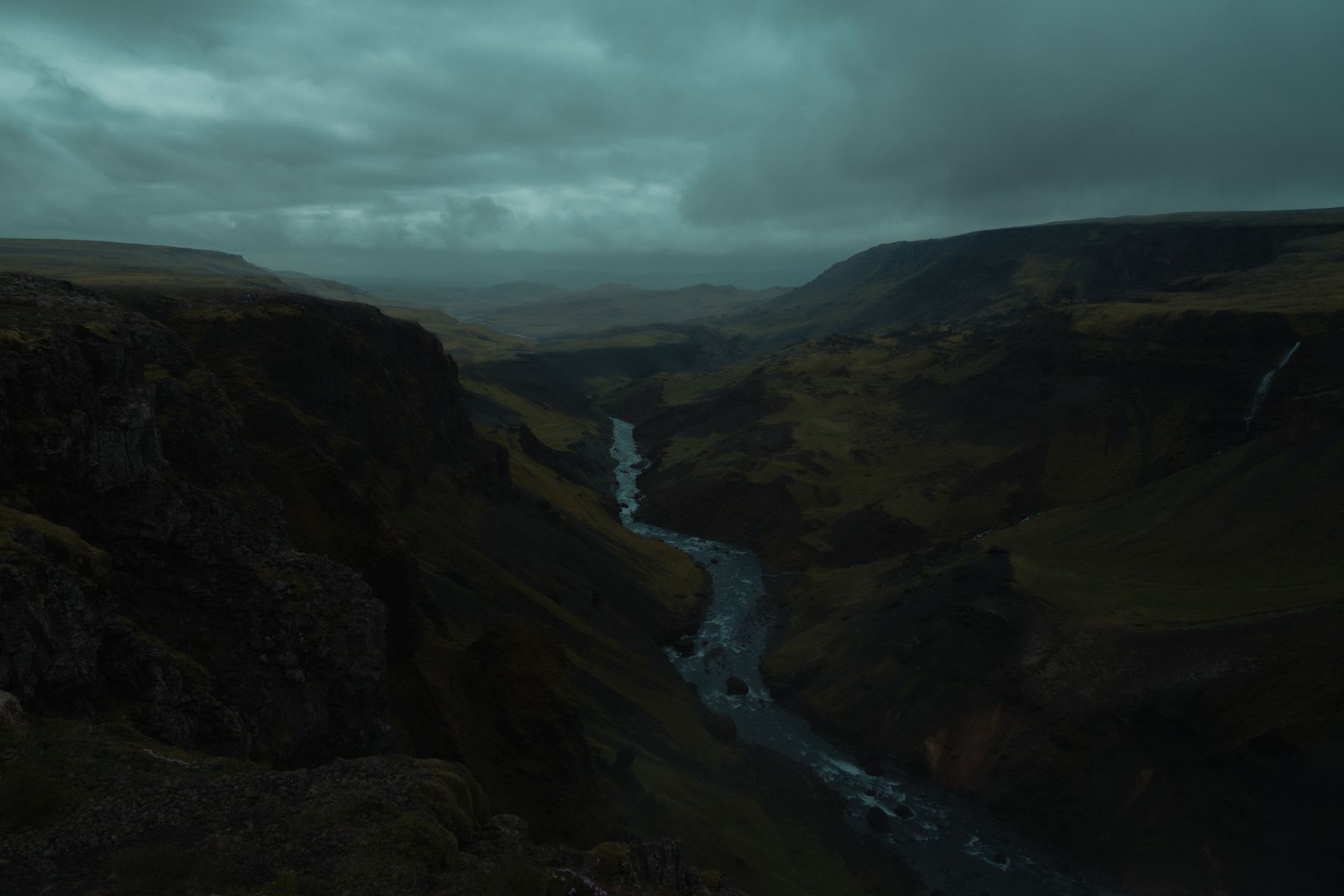 A dark and stormy sky over a mountain and a river in a natural landscape