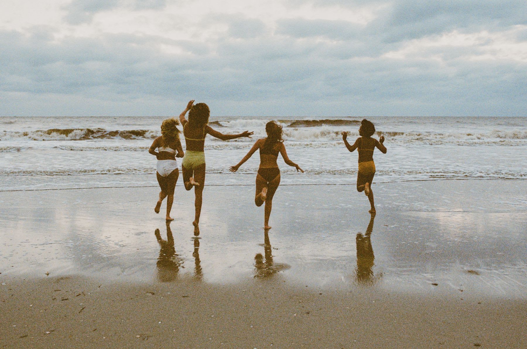 Four young girls on the beach running towards the water.