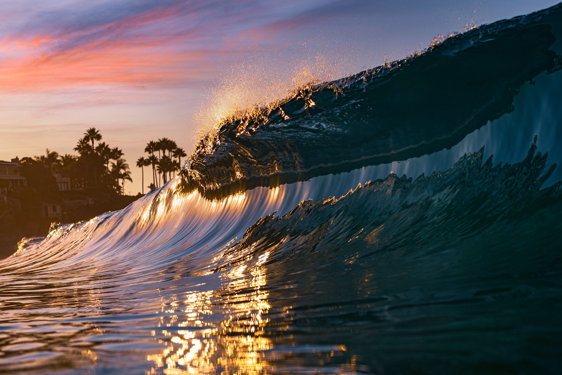 Waves rising high and curling creating splashes at the top as the dusk sun reflects off the water