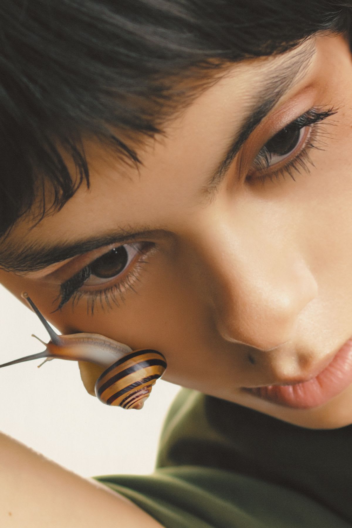 A snail with a striped shell on a models cheek close to her eye