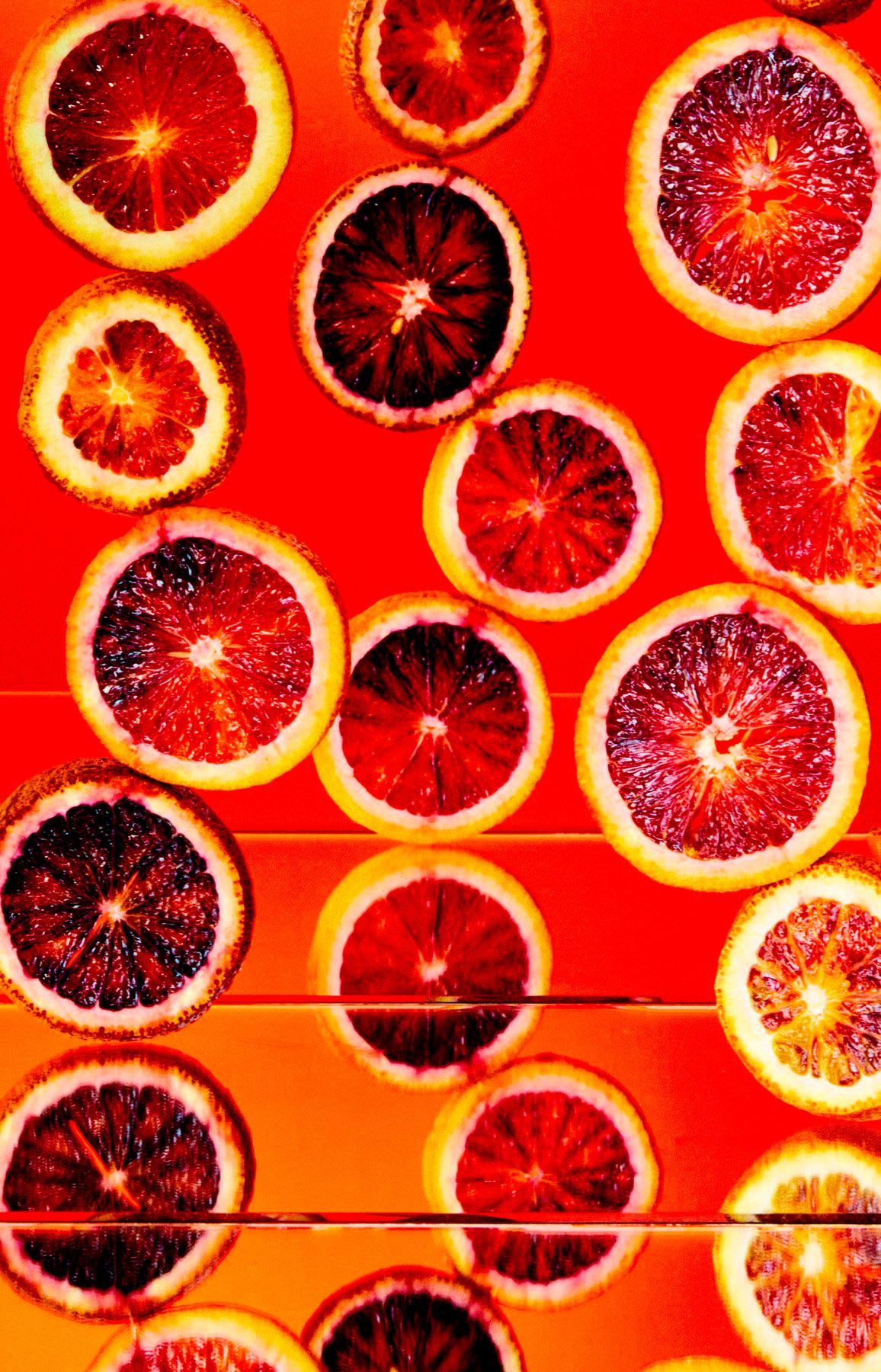 Red pulp of sliced citrus fruits matches the color of the surface the fruits rest on.