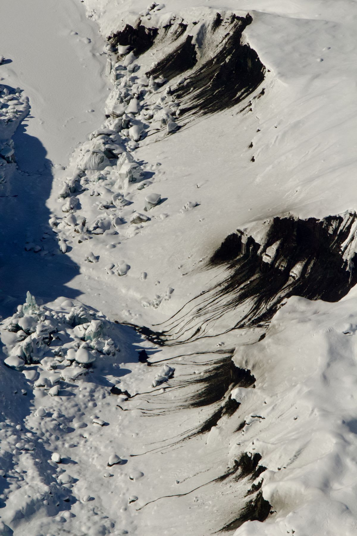 Aerial of a snowy landscape with stretches of exposed dark rock.