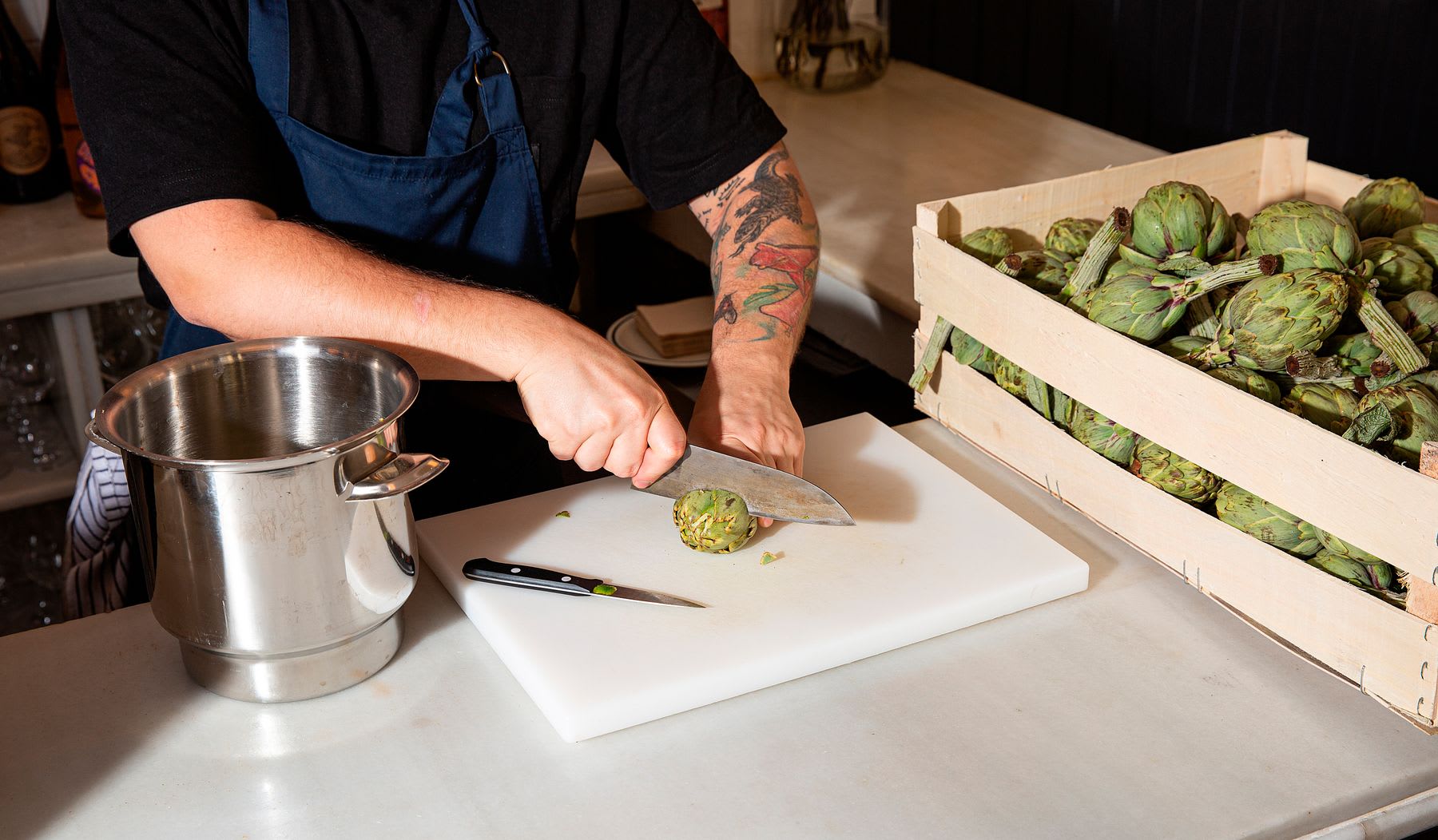 Man standing in a kitchen holding a knife as he cuts an artichoke