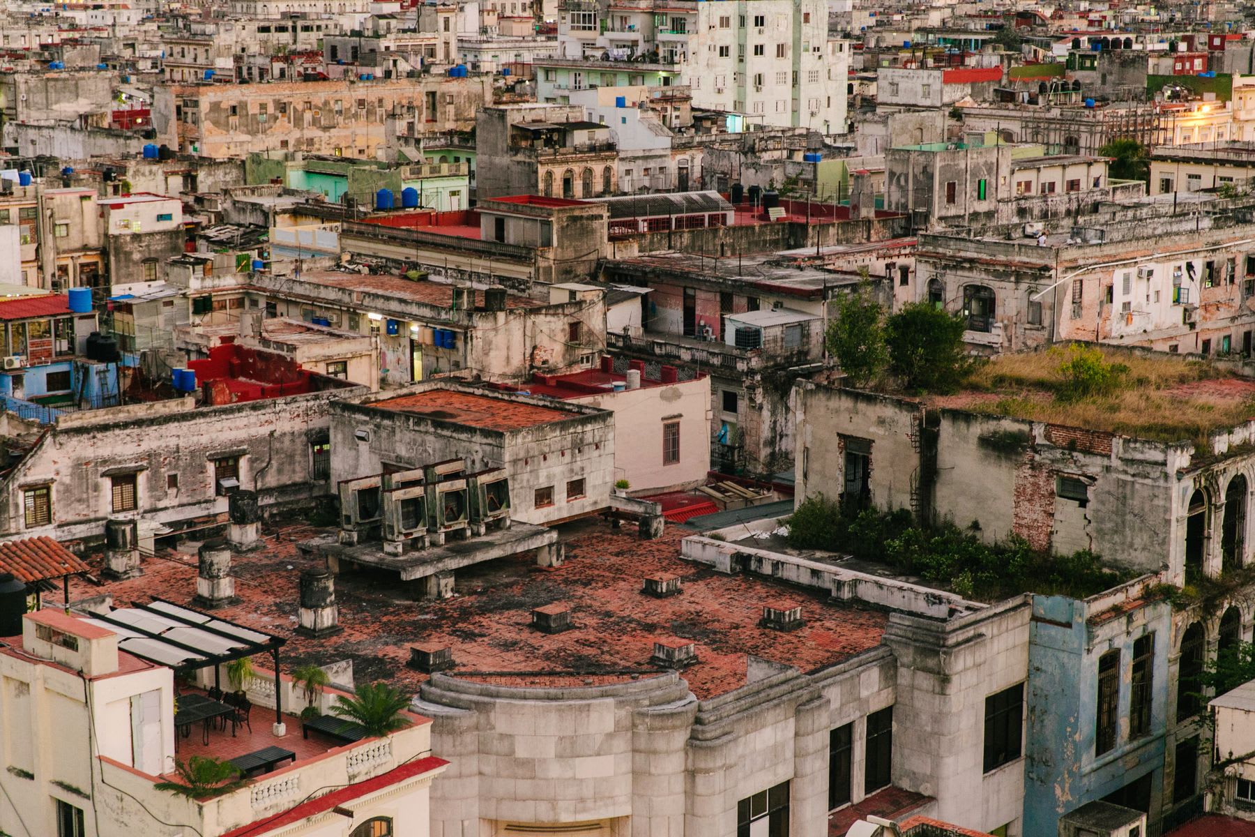an aerial view of Old Havana, Cuba, with a dense collection of buildings featuring varied textures and colors, including red and green roofs, and a cityscape in the background.
