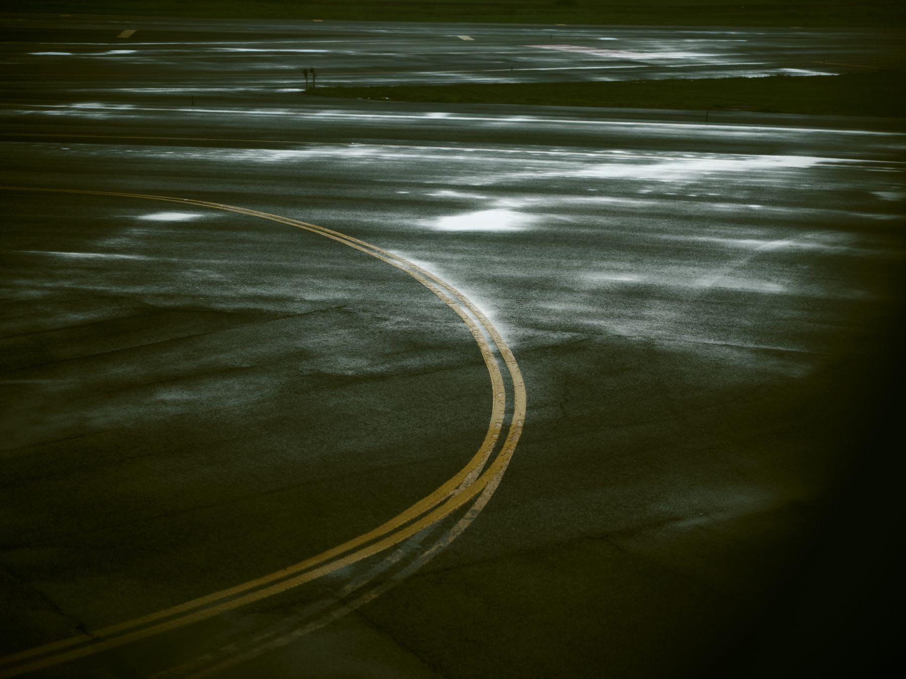 A wet airport tarmac glistens under the light, with curved yellow taxiway lines guiding the path across the expansive airfield.