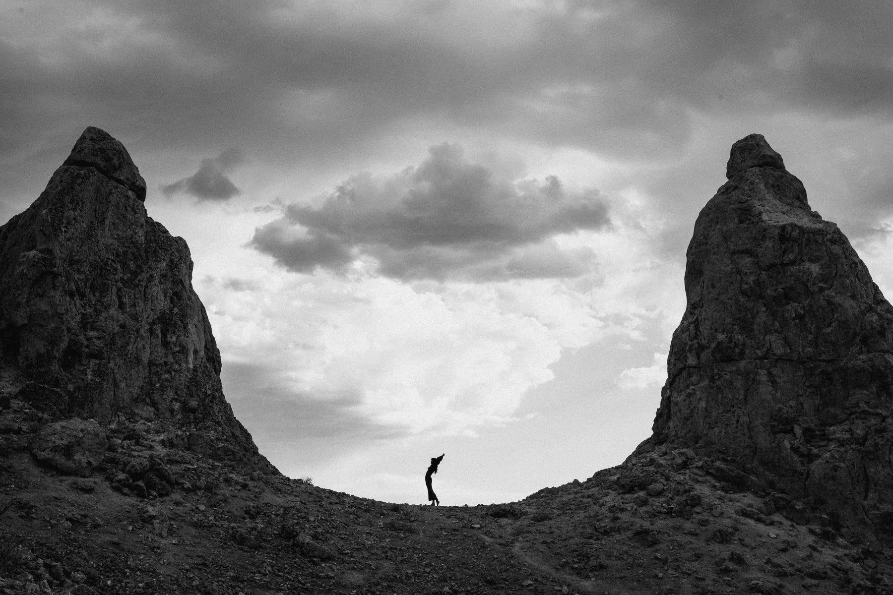 Woman standing between two tall rock formations silhouetted against a cloudy sky