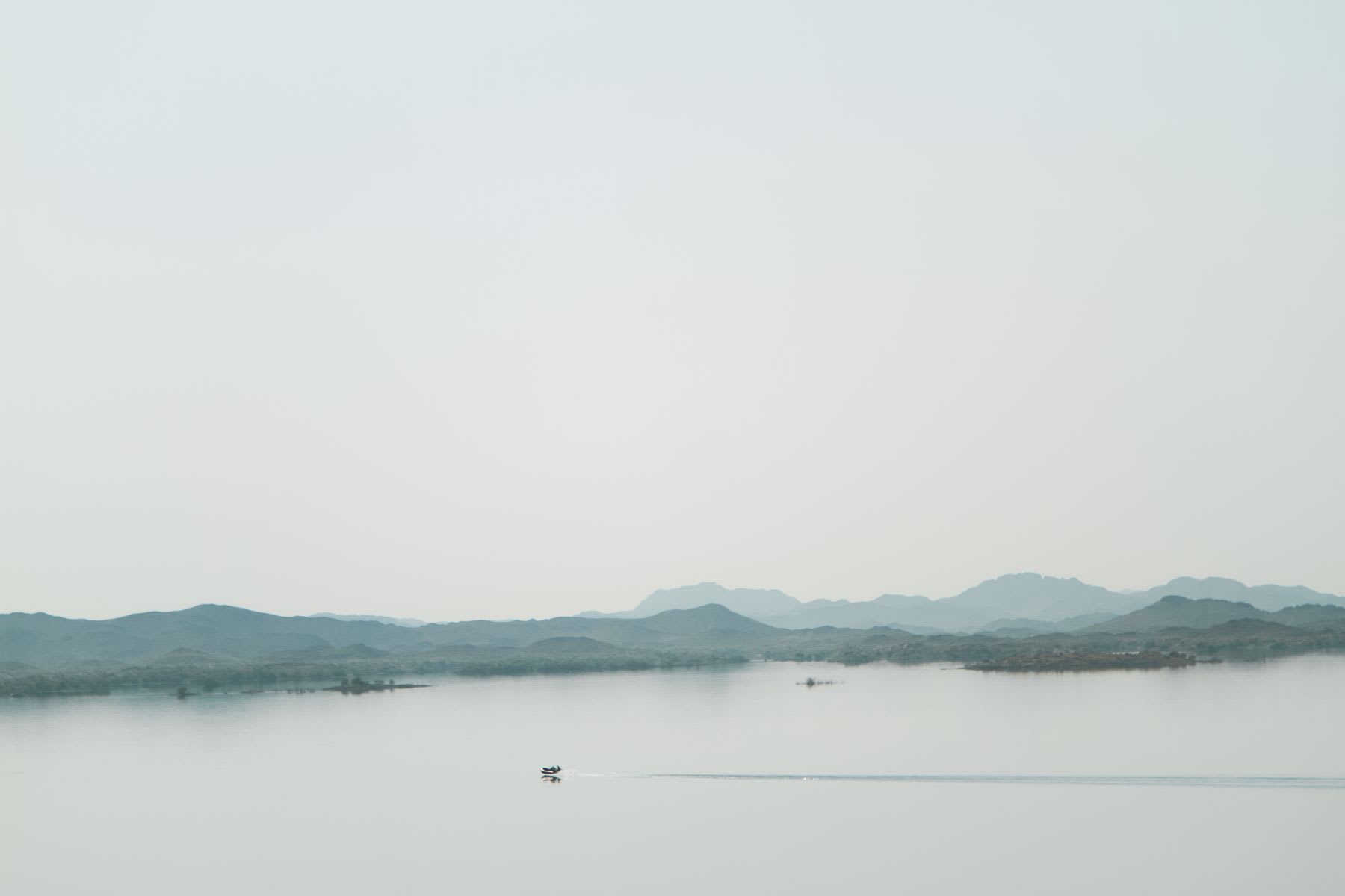 A boat travels across a still lake with mountains rising in the background.