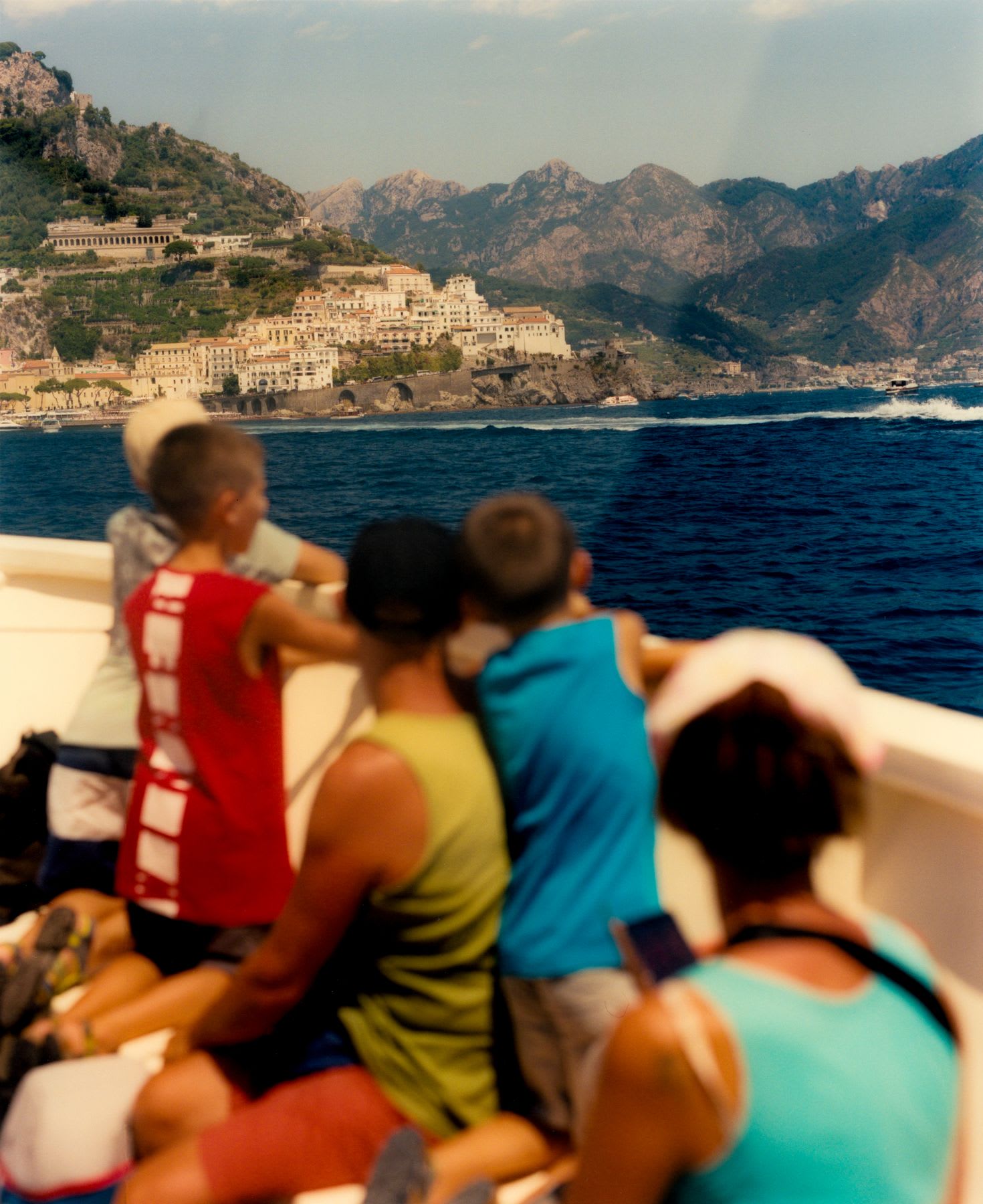 A family sits in a boat overlooking the ocean on a summer day.