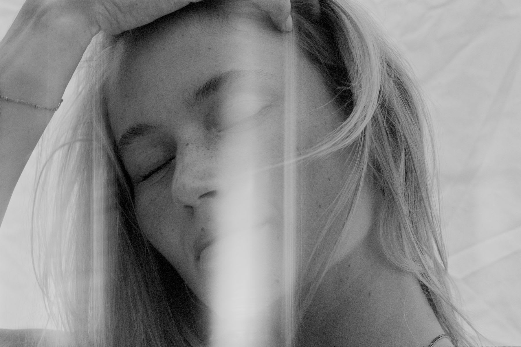 Close-up of a young blonde woman's face with her eyes shut and a hand over her forehead.